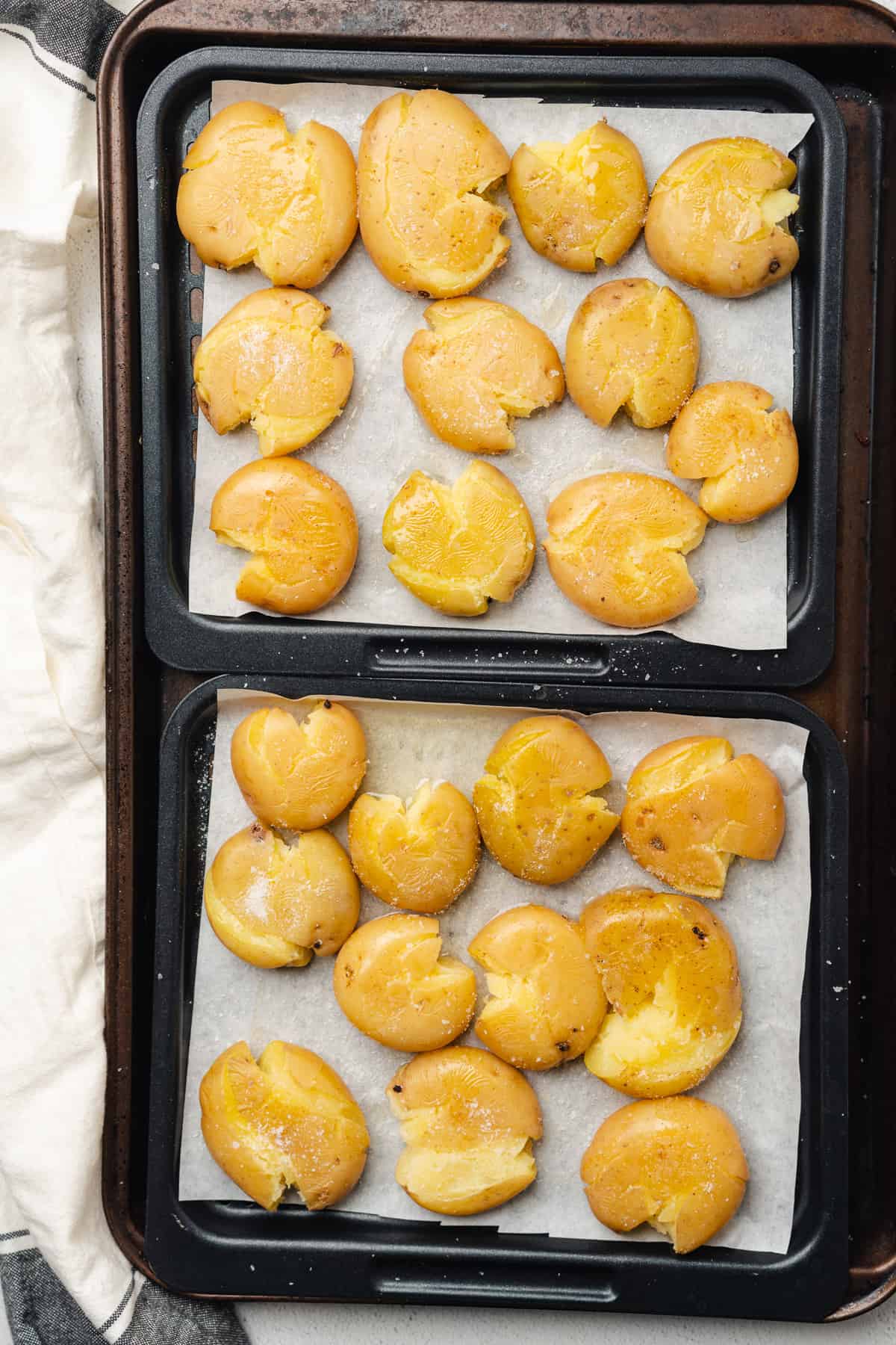 smashed baby golden potatoes on an air fryer tray with parchment, oil and salt