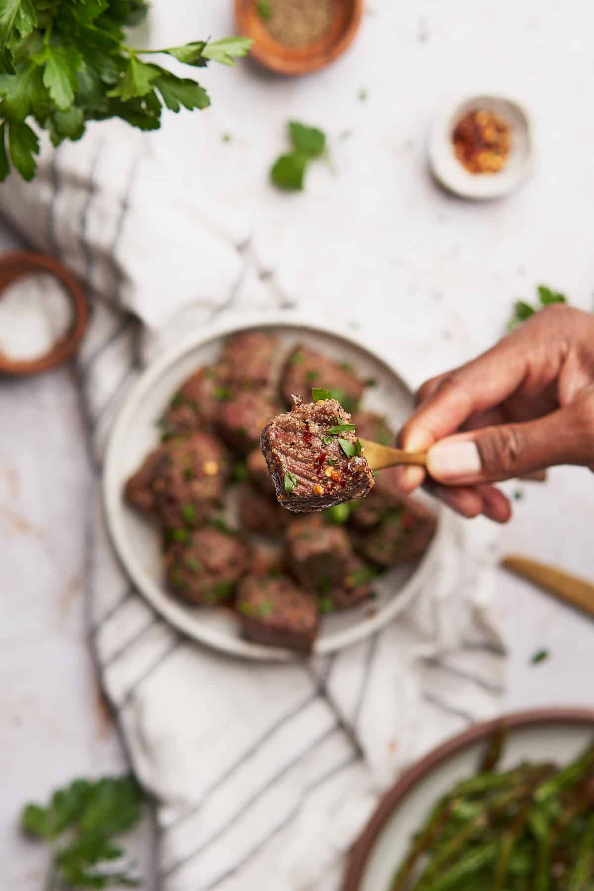 steak garnished with parsley, being held on a gold fork over a white background.