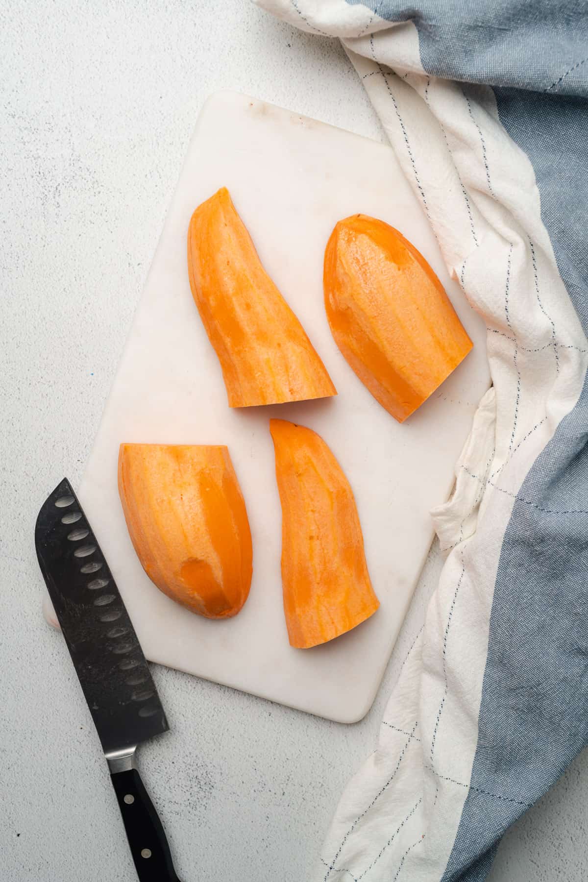 sweet potato cut into 4 pieces on a cutting board with a sharp knife nearby