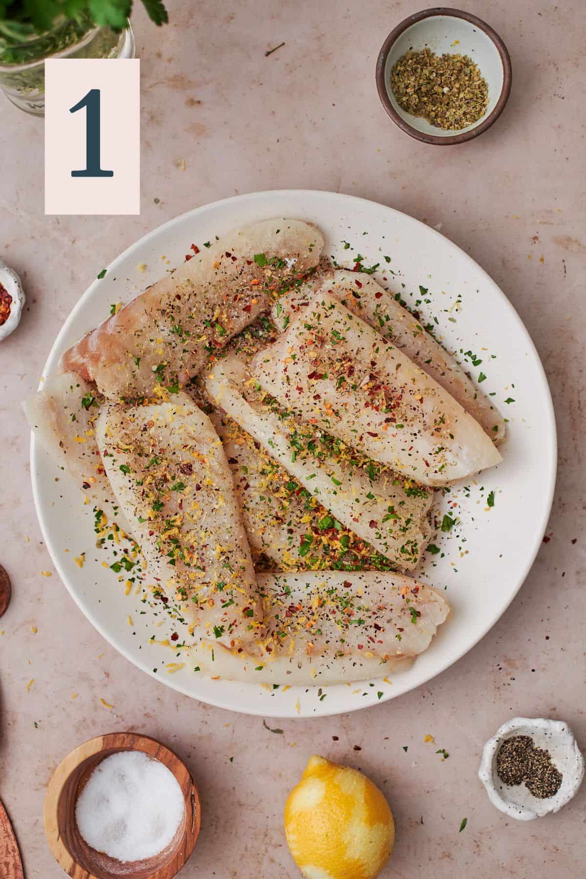 seasoned cod filets on a plate with lemon zest, red pepper flakes, parsley, salt, and pepper. 