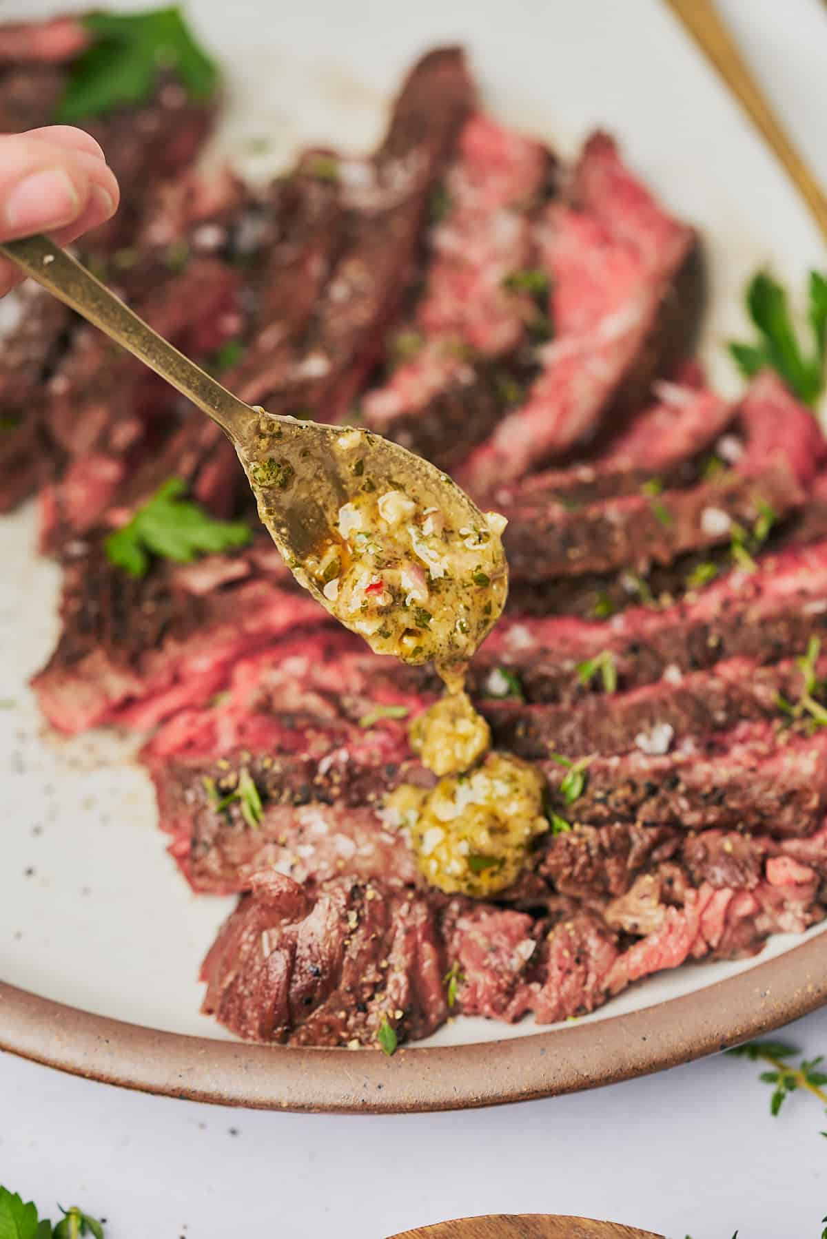 spoon drizzling garlic herb butter over top of a bavette steak.