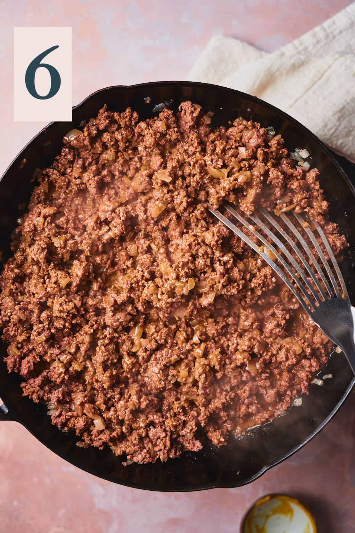 Cooked ground beef in a skillet with a metal spatula. 