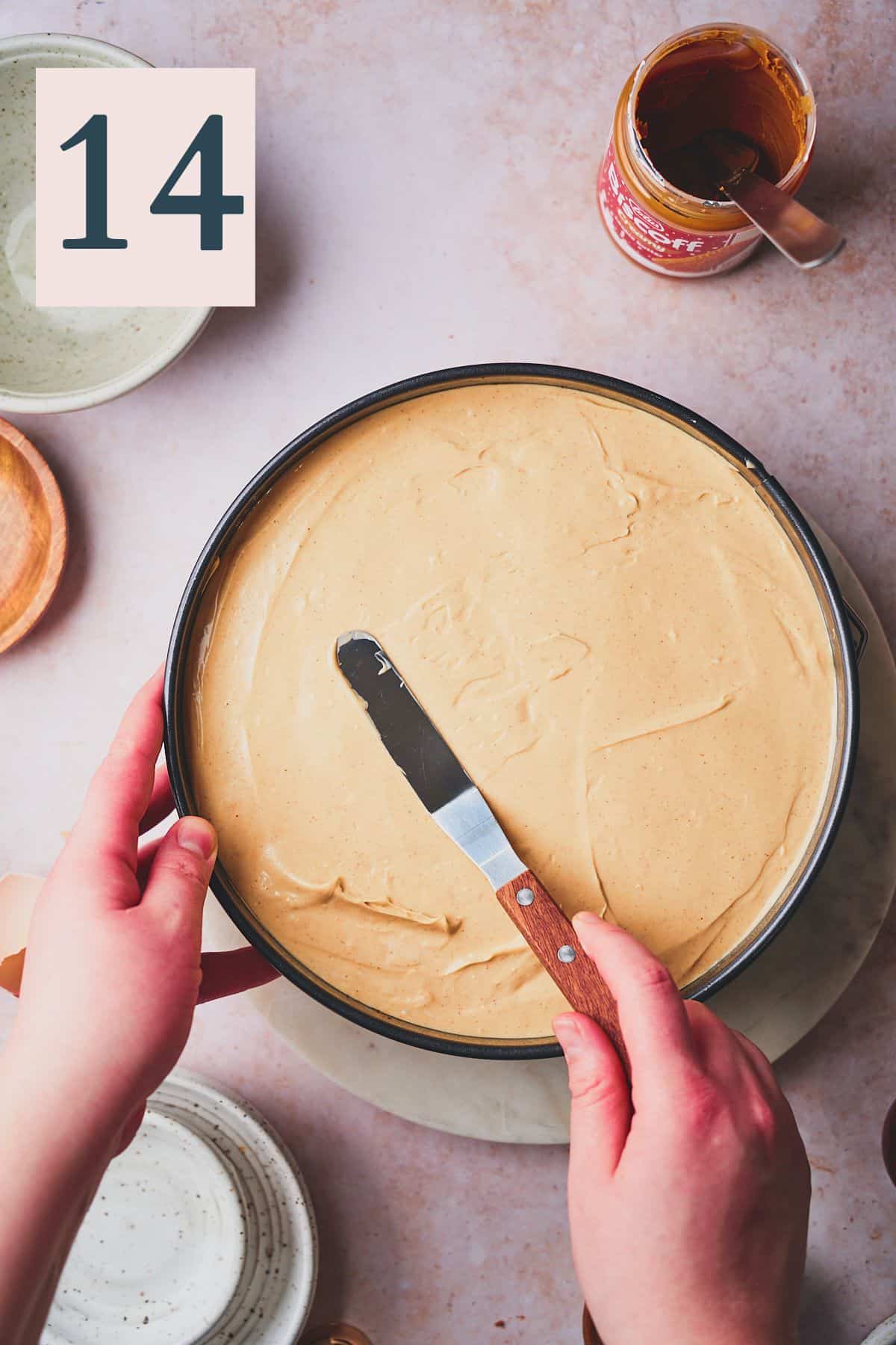 Hand spreading cheesecake batter in a springform pan with an offset spatula. 