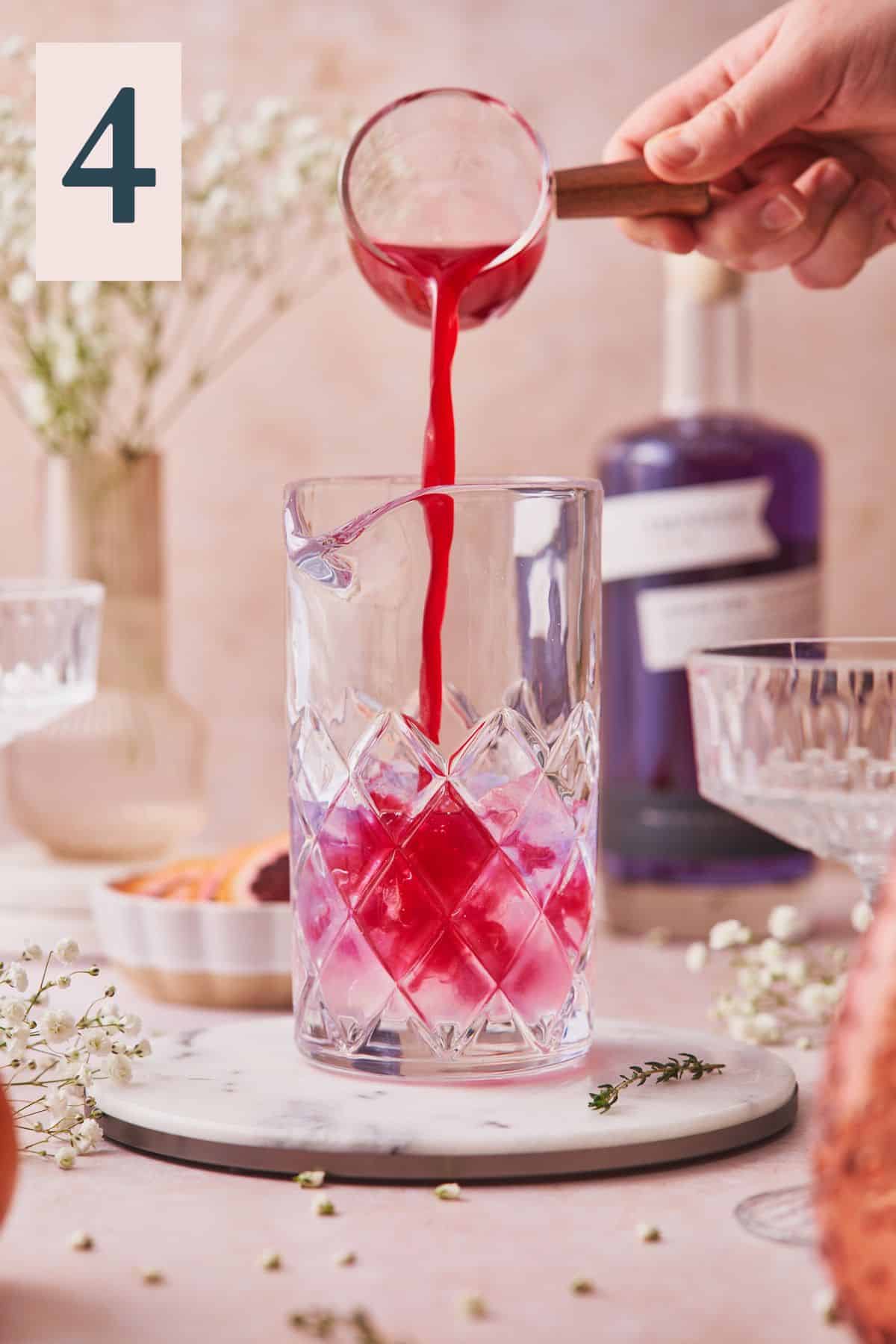 hand pouring bright red blood orange juice into a mixing glass with other ingredients to make a gin cocktail. 