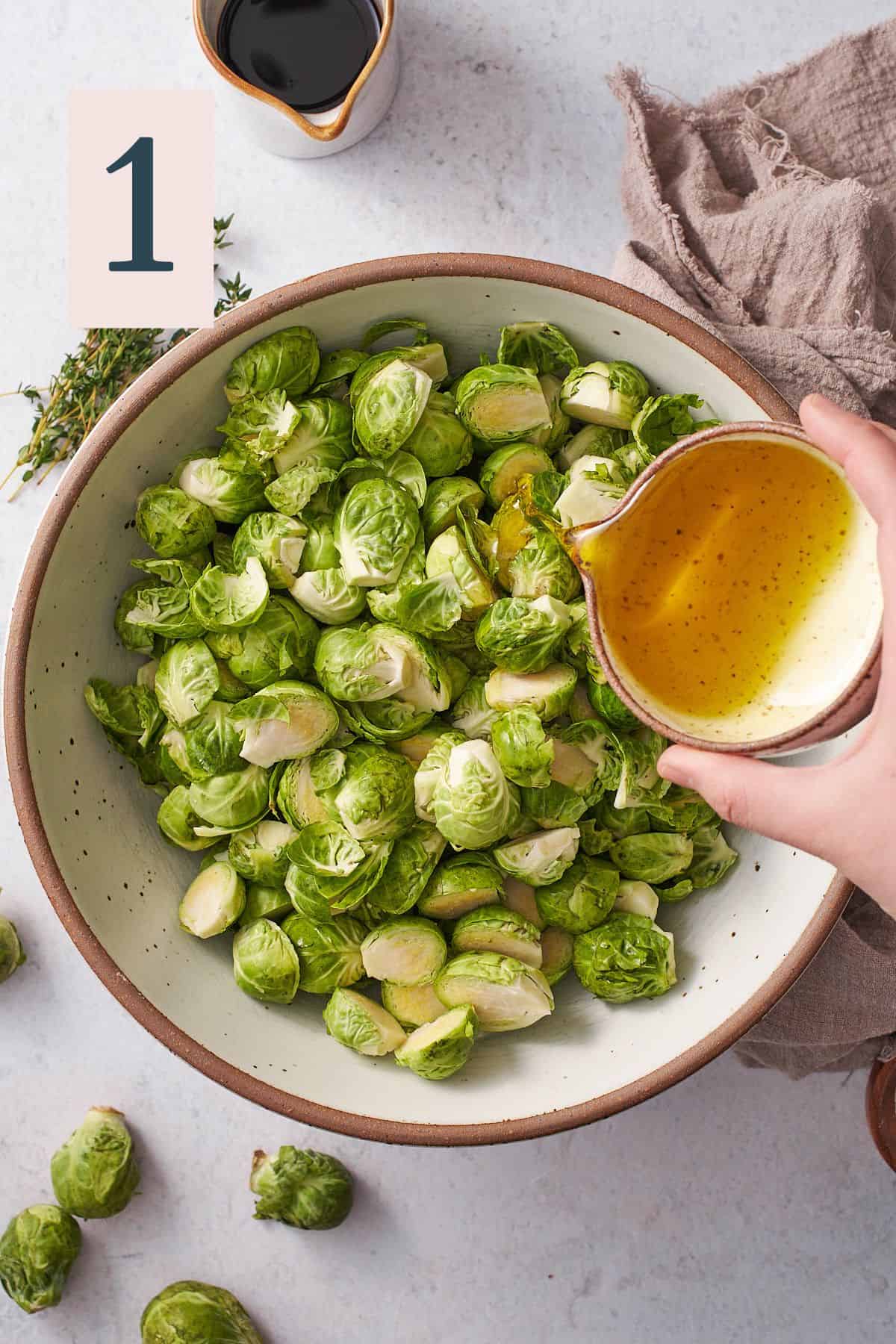 hand pouring olive oil into a large bowl of halved brussel sprouts. 