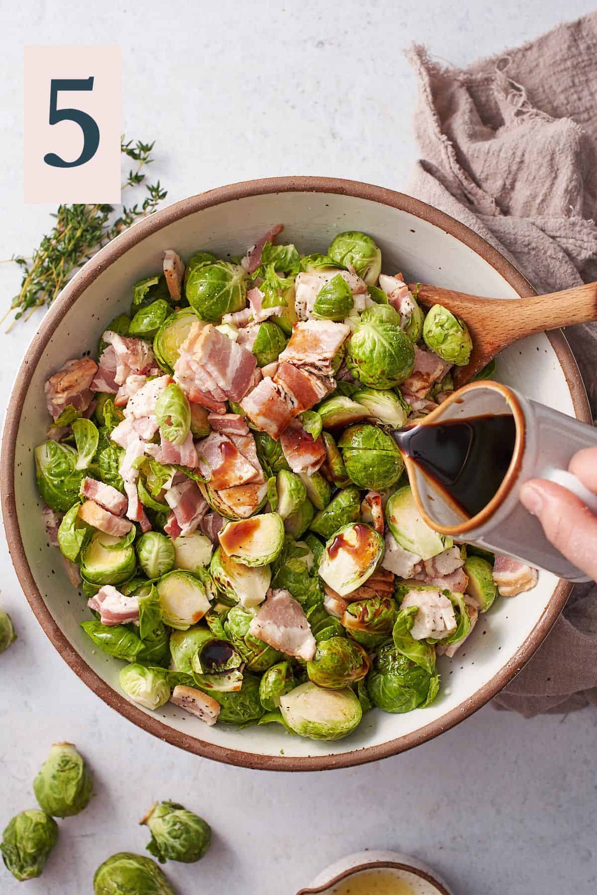 hand pouring balsamic vinegar into a bowl of brussels sprouts and bacon