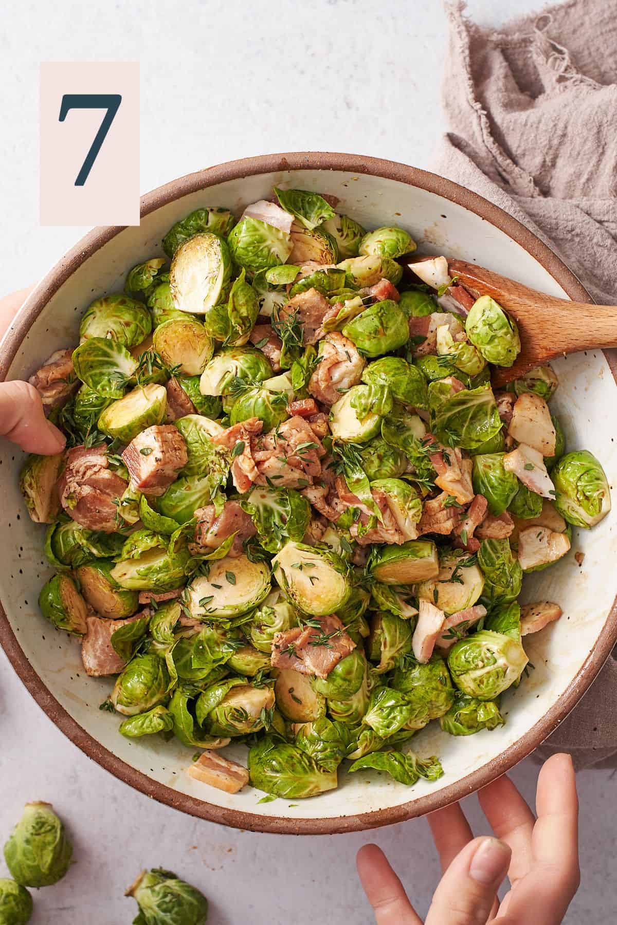 raw brussels sprouts and bacon in a bowl with other ingredients tossed together, and wooden spoon inside the bowl. 
