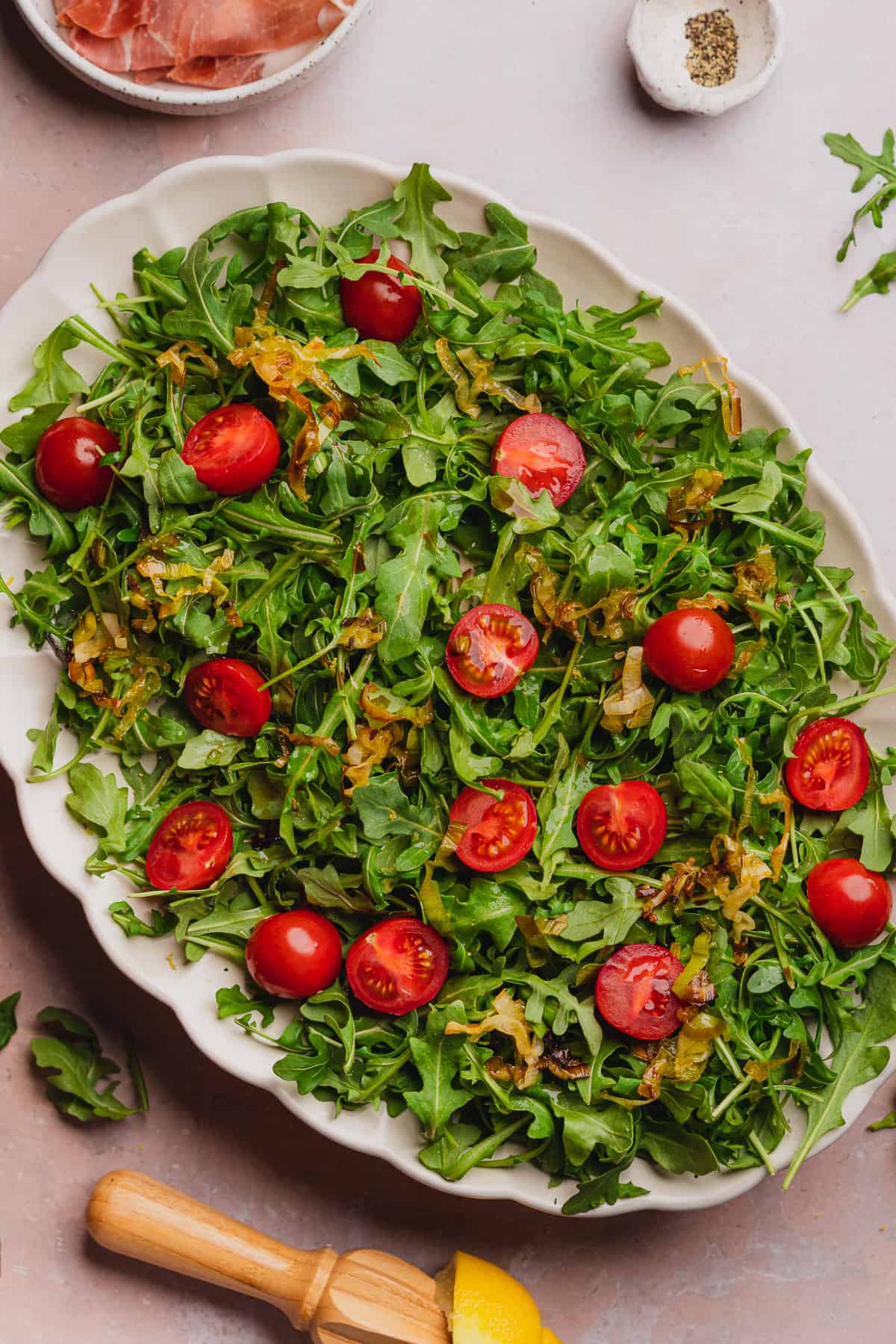 halved cherry tomatoes on a bed of arugula with fried leeks