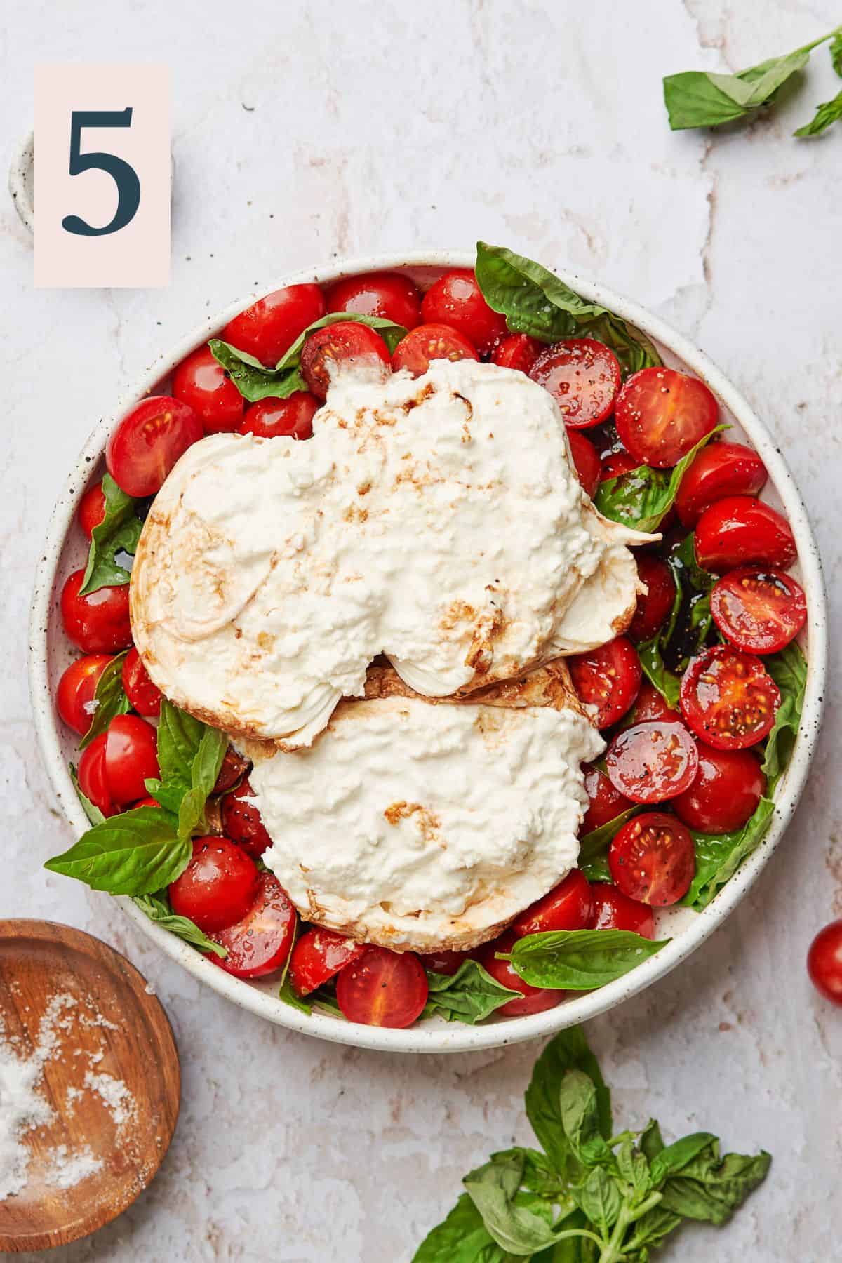Burrata cheese broken open with a spoon or knife to evenly distribute over salad.