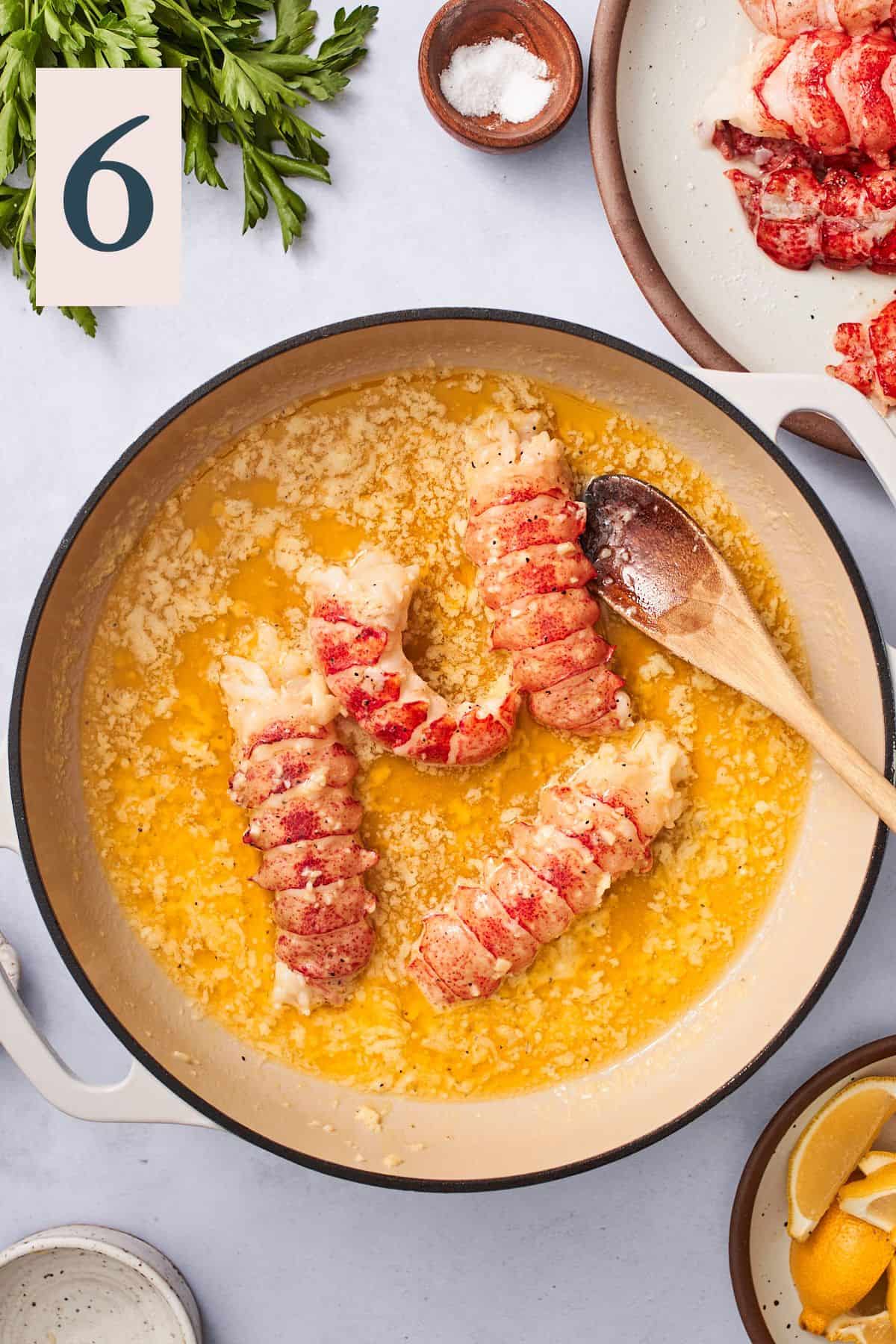 cooked lobster tails, with tails beginning to curl in a pan of buttery liquid. 