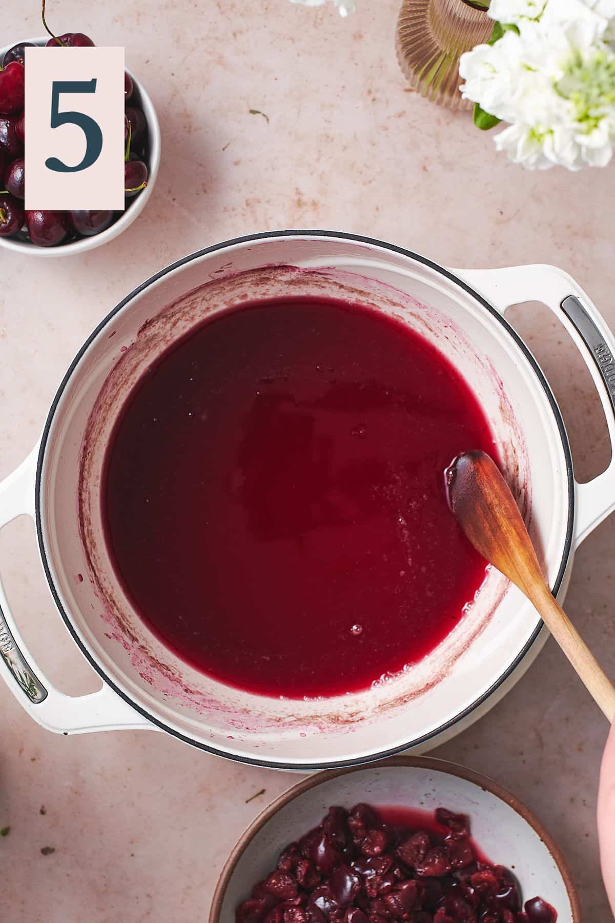 cherry juice liquid in an enameled cast iron dutch oven, with a spoon in it to stir. 