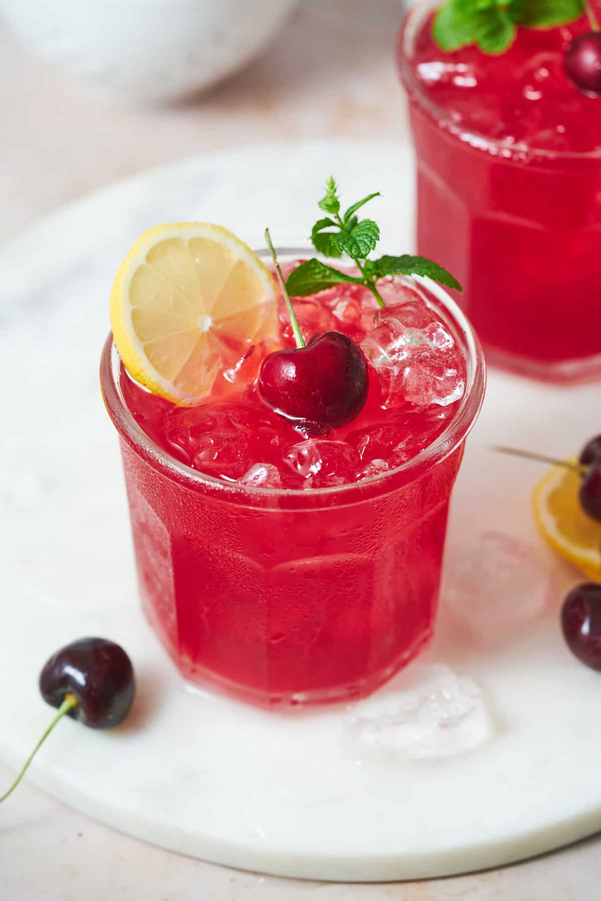 cherry lemonade in a cute jar, topped with a mint sprig, fresh lemon slices and a cherry on a stem.