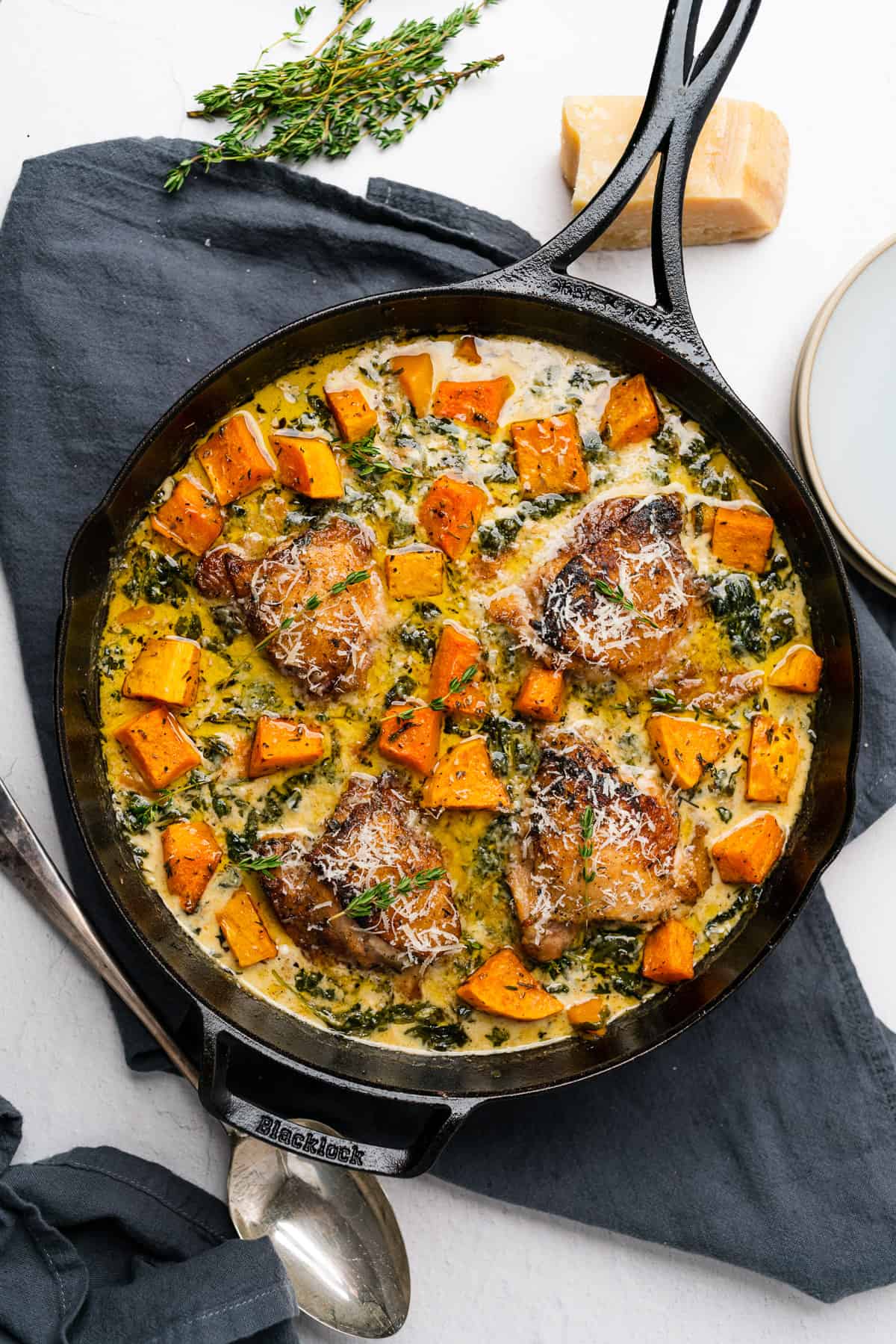Overhead shot of chicken and butternut squash recipe skillet with towel and spoon