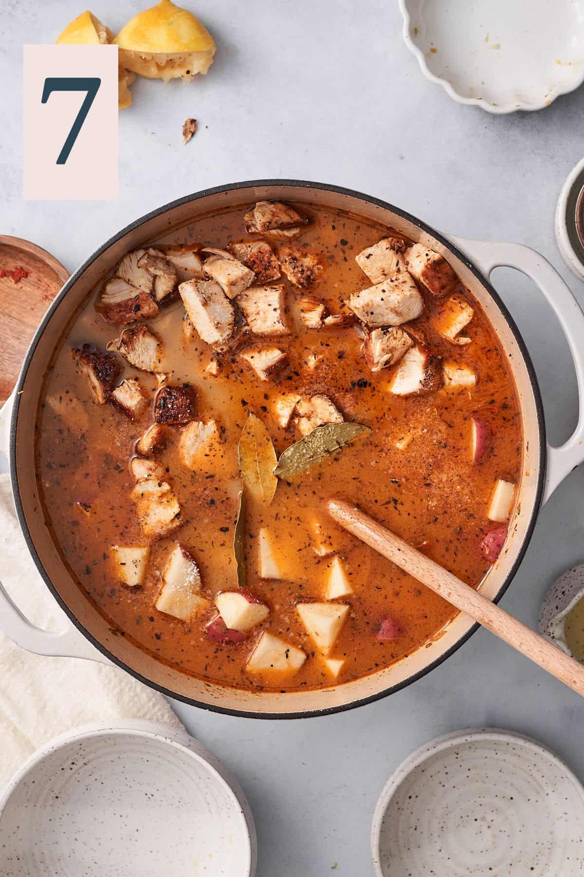pot full of broth with vegetables, chicken pieces, and potatoes. 