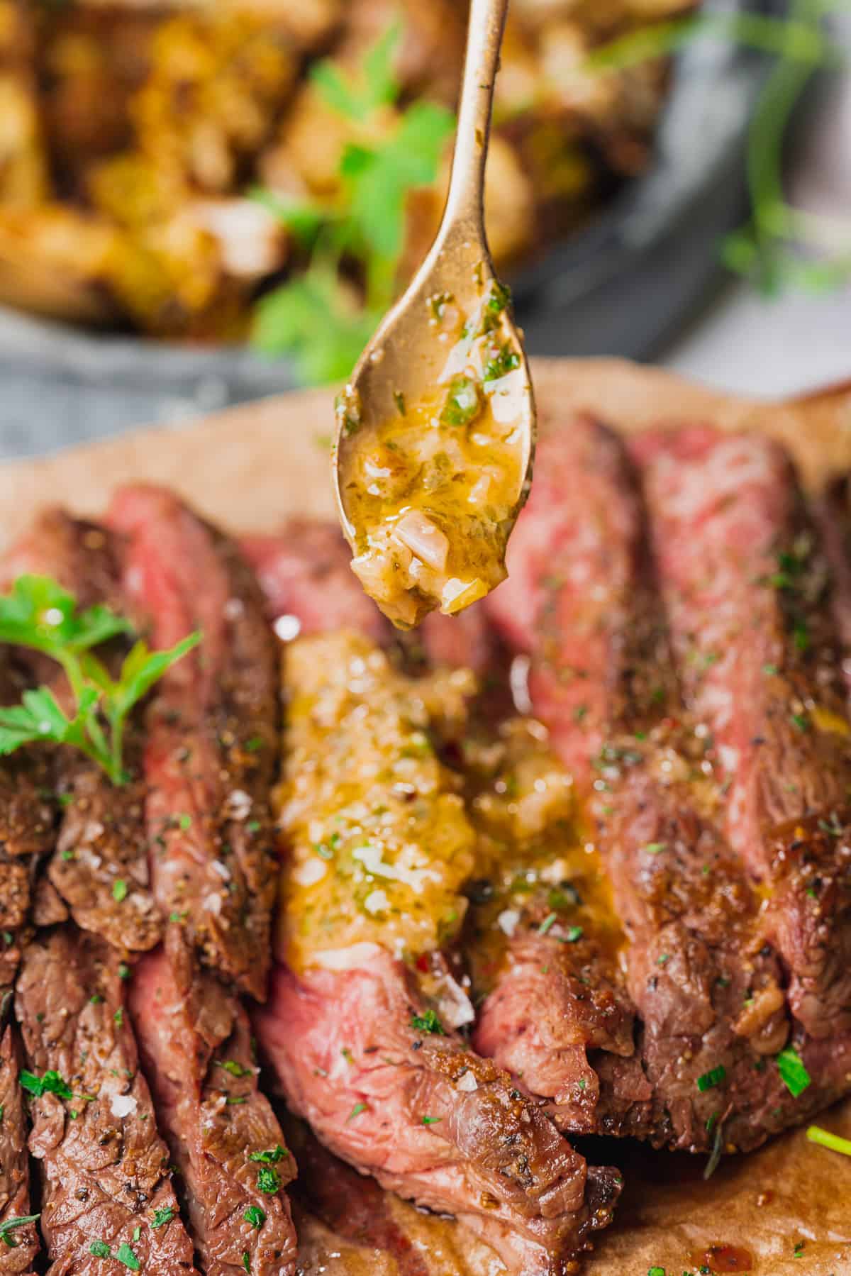 spoonful of cowboy butter dipping sauce being drizzled onto medium rare sliced steak. 