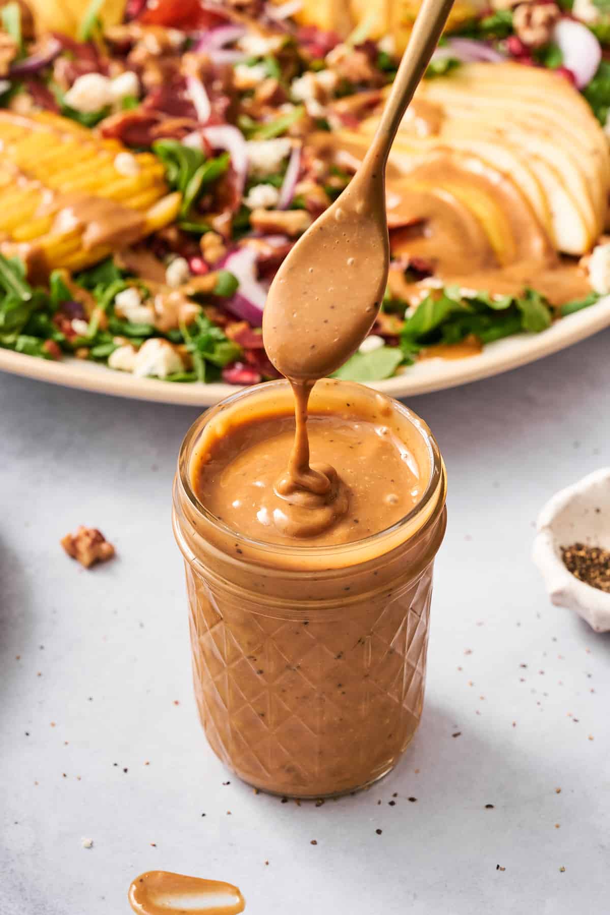 delicious creamy balsamic dressing in a jar, falling off a spoon with a pear and arugula salad in the background. 