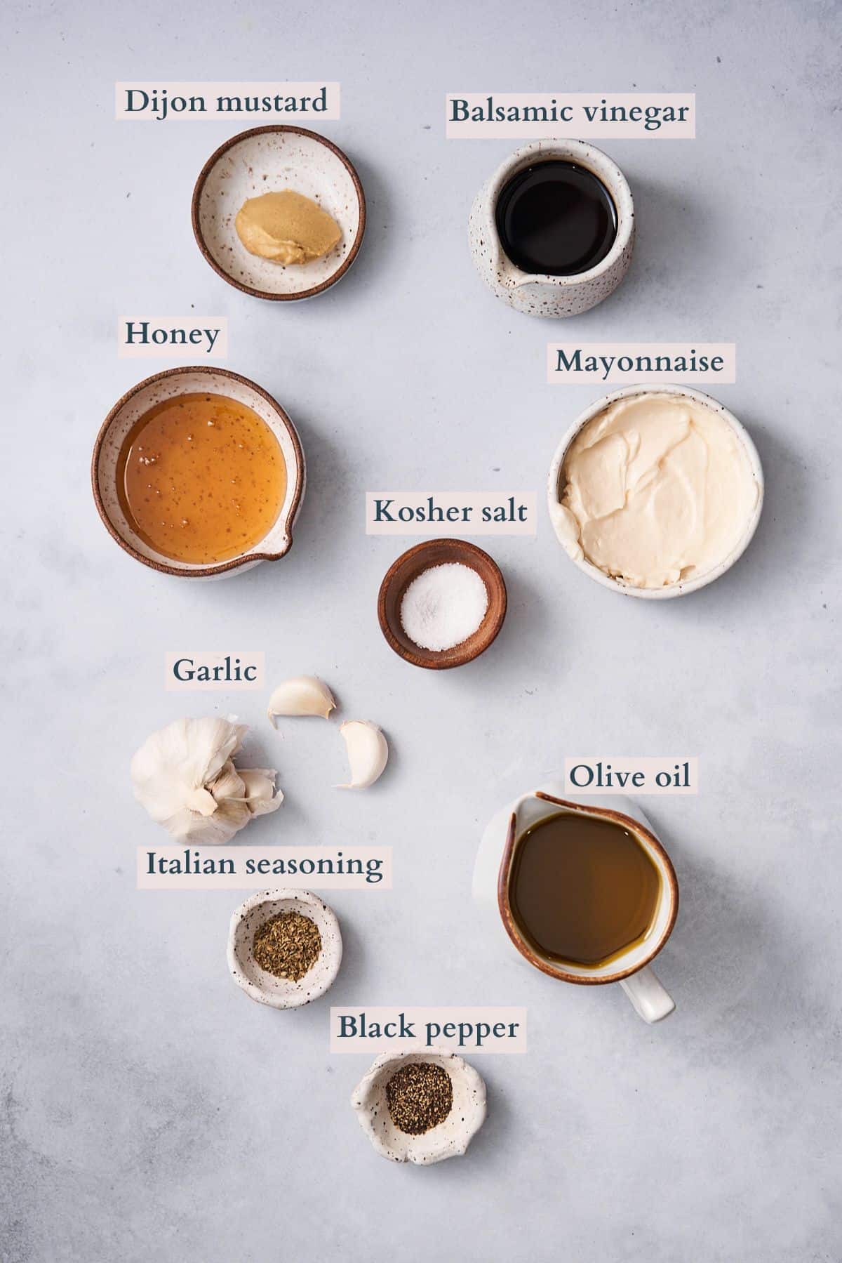 ingredients to make the creamy balsamic dressing laid out in small ceramic bowls with text overlaying to denote each ingredient.