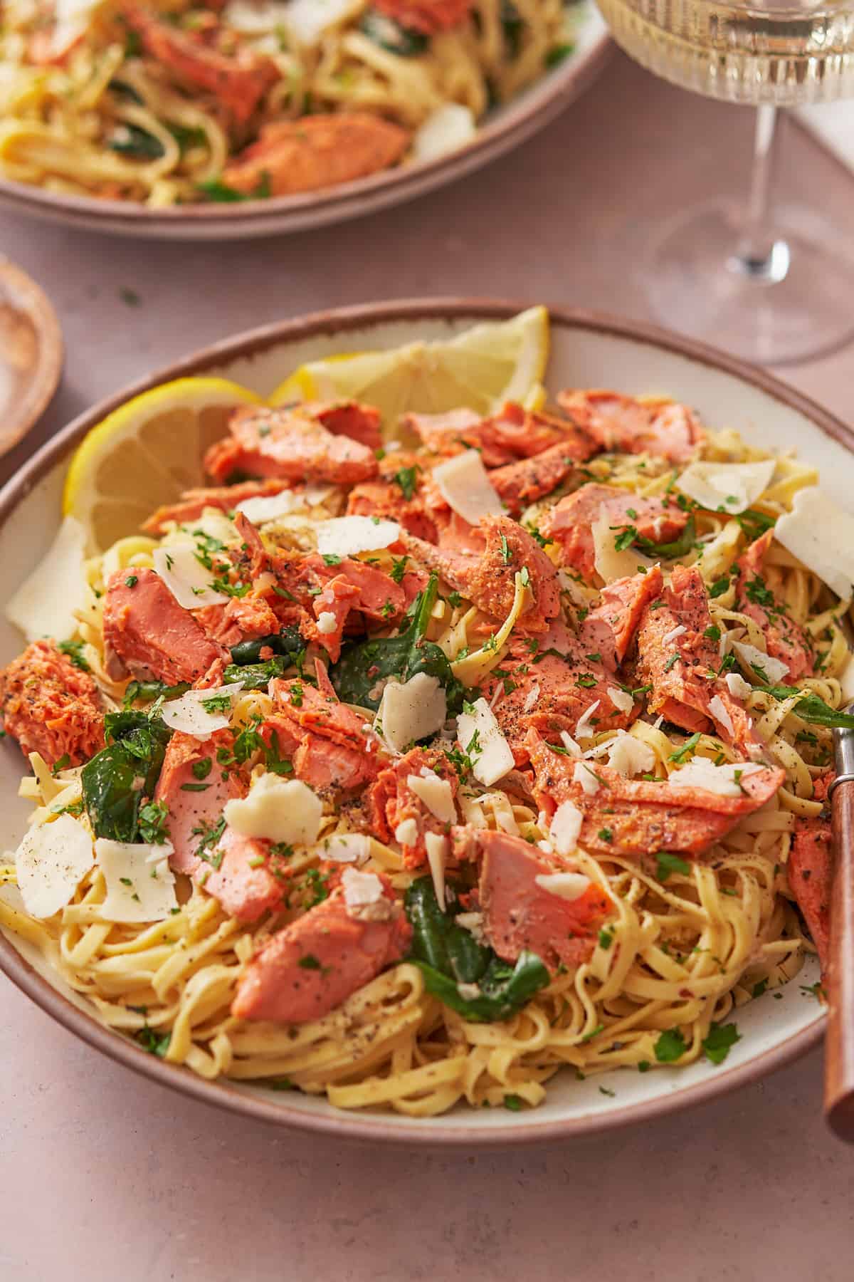 large bowl of creamy salmon pasta with large bites of salmon, spinach, and lemons.