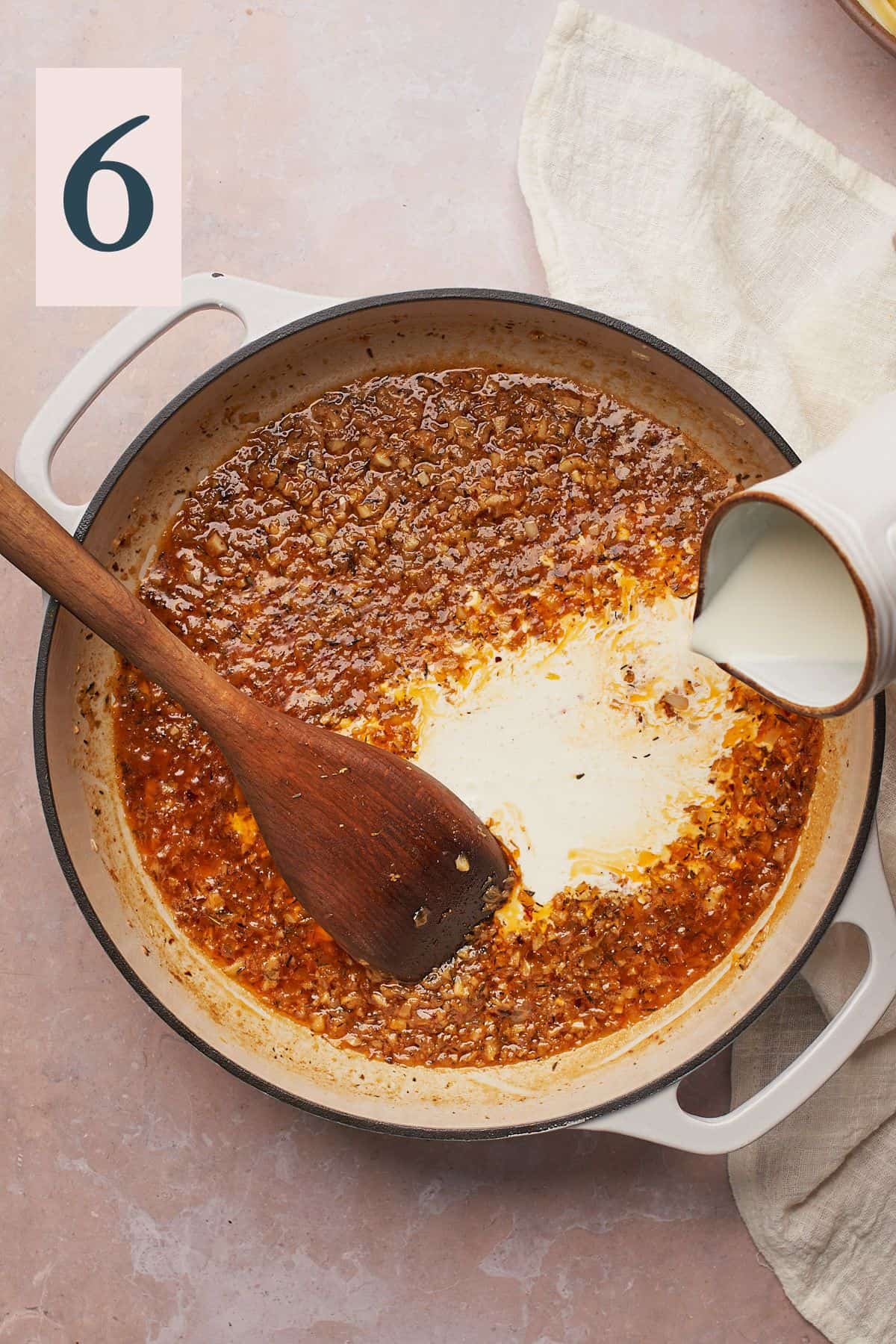 pouring cream into an enameled cast iron skillet with cooked onions, garlic and seasonings.