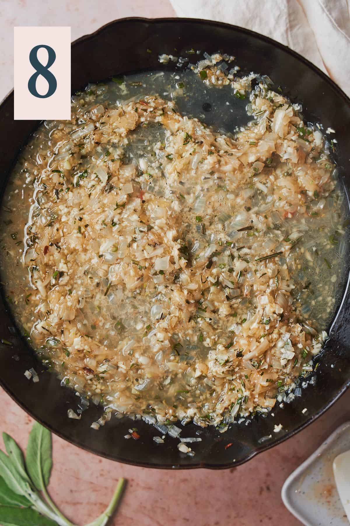 Cooked onions, garlic, and herbs in a skillet with chicken broth. 