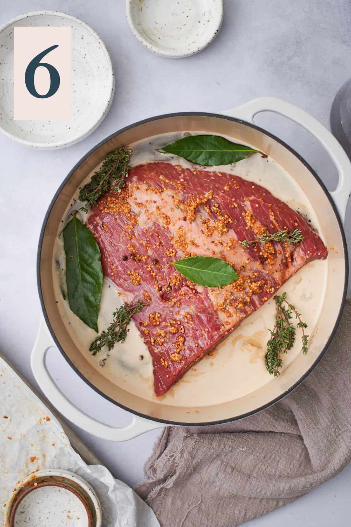 raw corned beef brisket in an enameled dutch oven with beef stock, creamy guinness beer, bay leaves, and fresh thyme. 