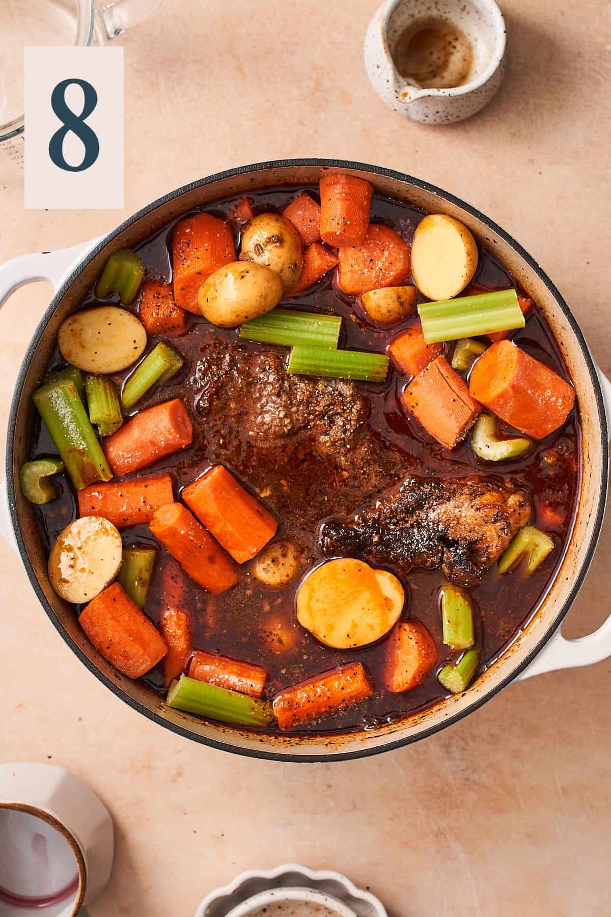 pot roast in braising liquid, with potatoes, celery and carrots added to the pot. 