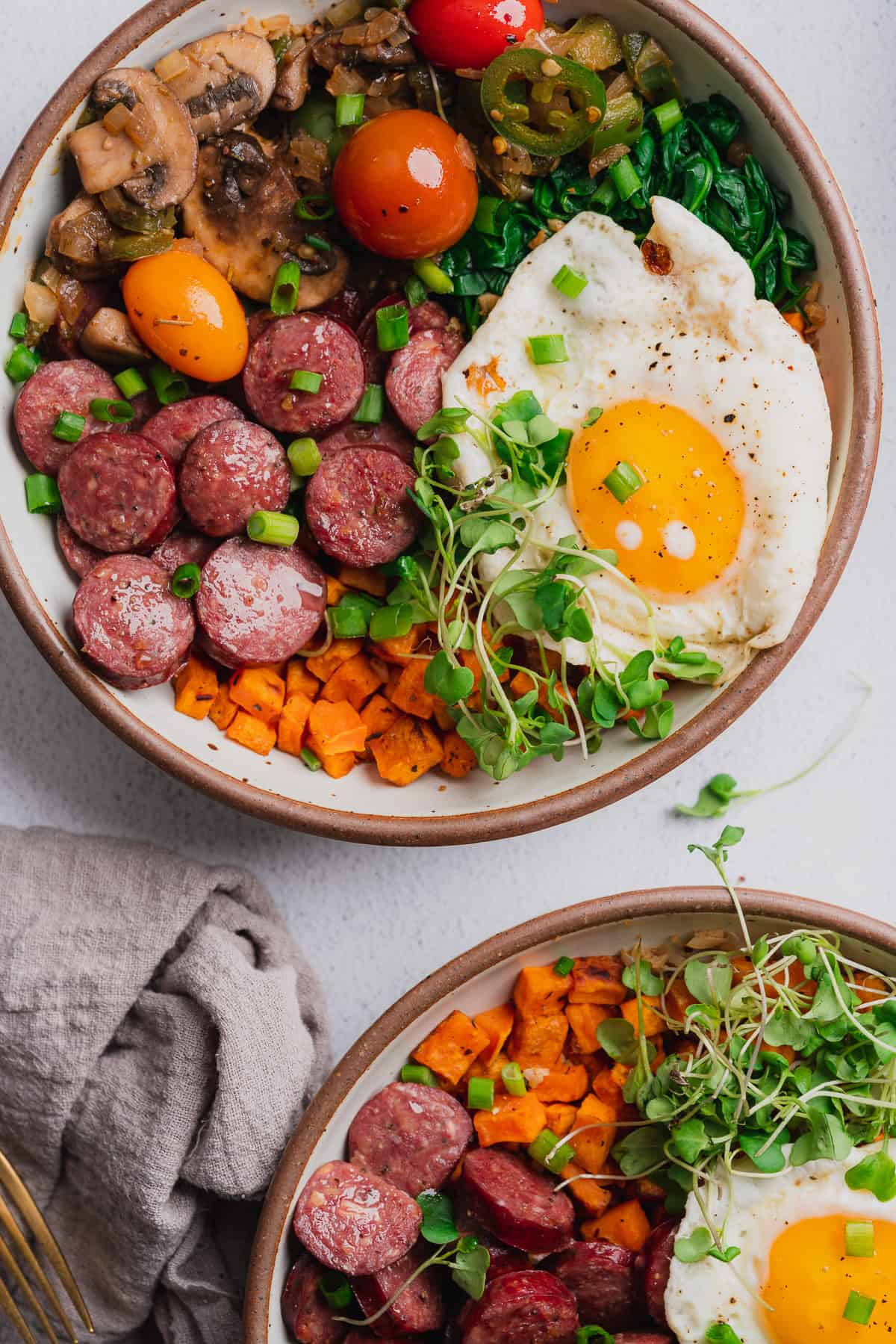 two lovely power energy bowls with lots of veggies, smoked sausage and broccoli greens and a fried egg