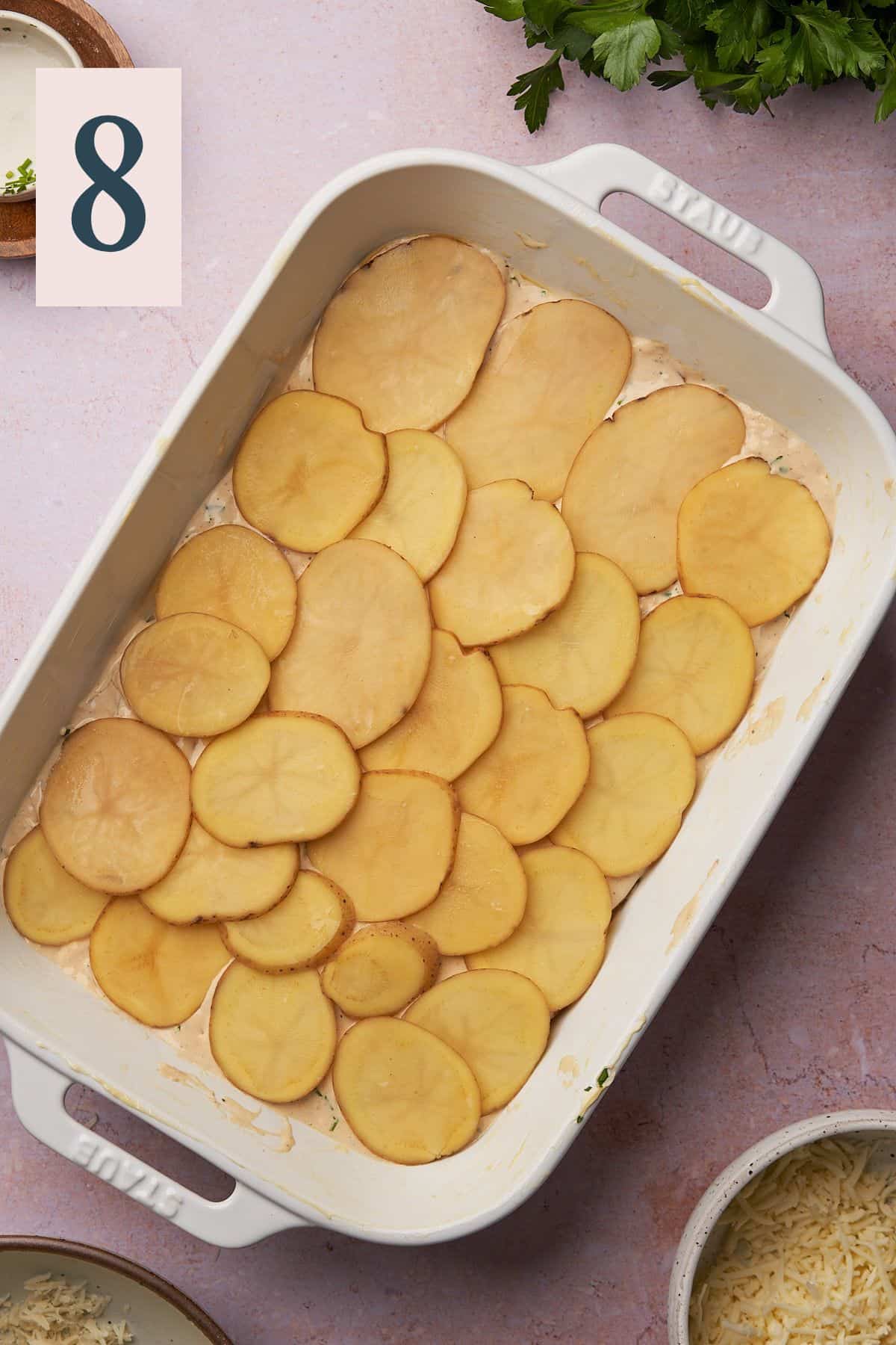 potato slices and cheese sauce being added to a casserole dish. 