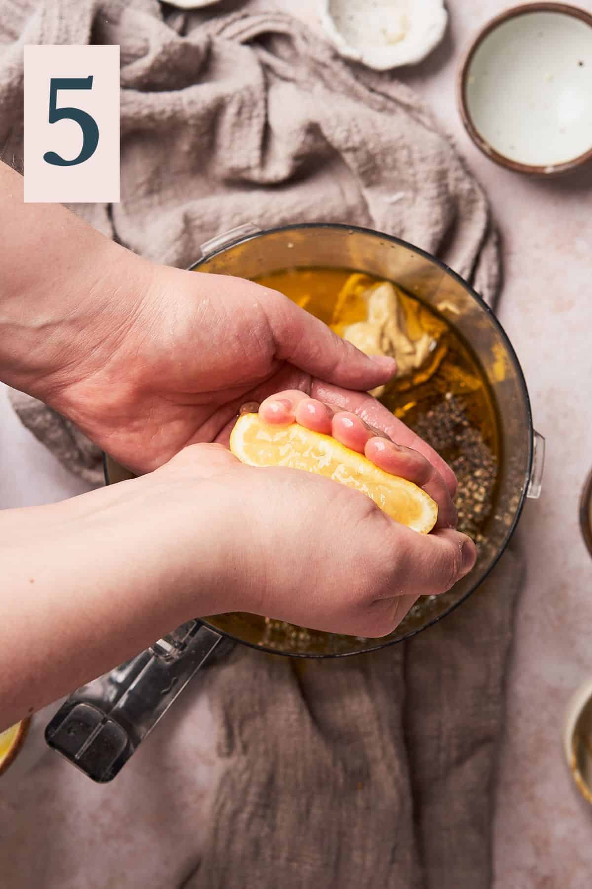 hand squeezing a lemon into a food processor to make a honey lemon dressing.