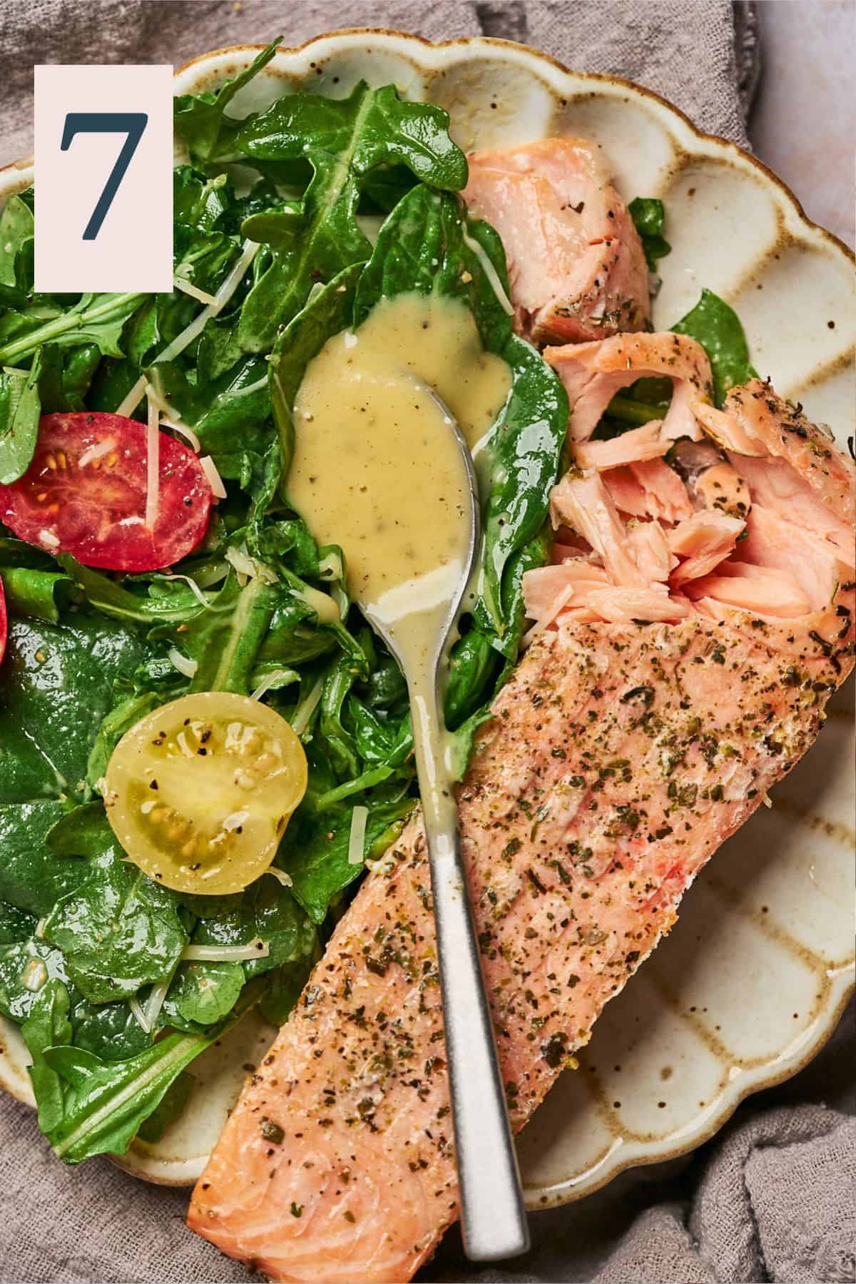 spoonful of honey lemon vinaigrette dressing on top of a simple arugula and spinach salad, with a side of salmon.