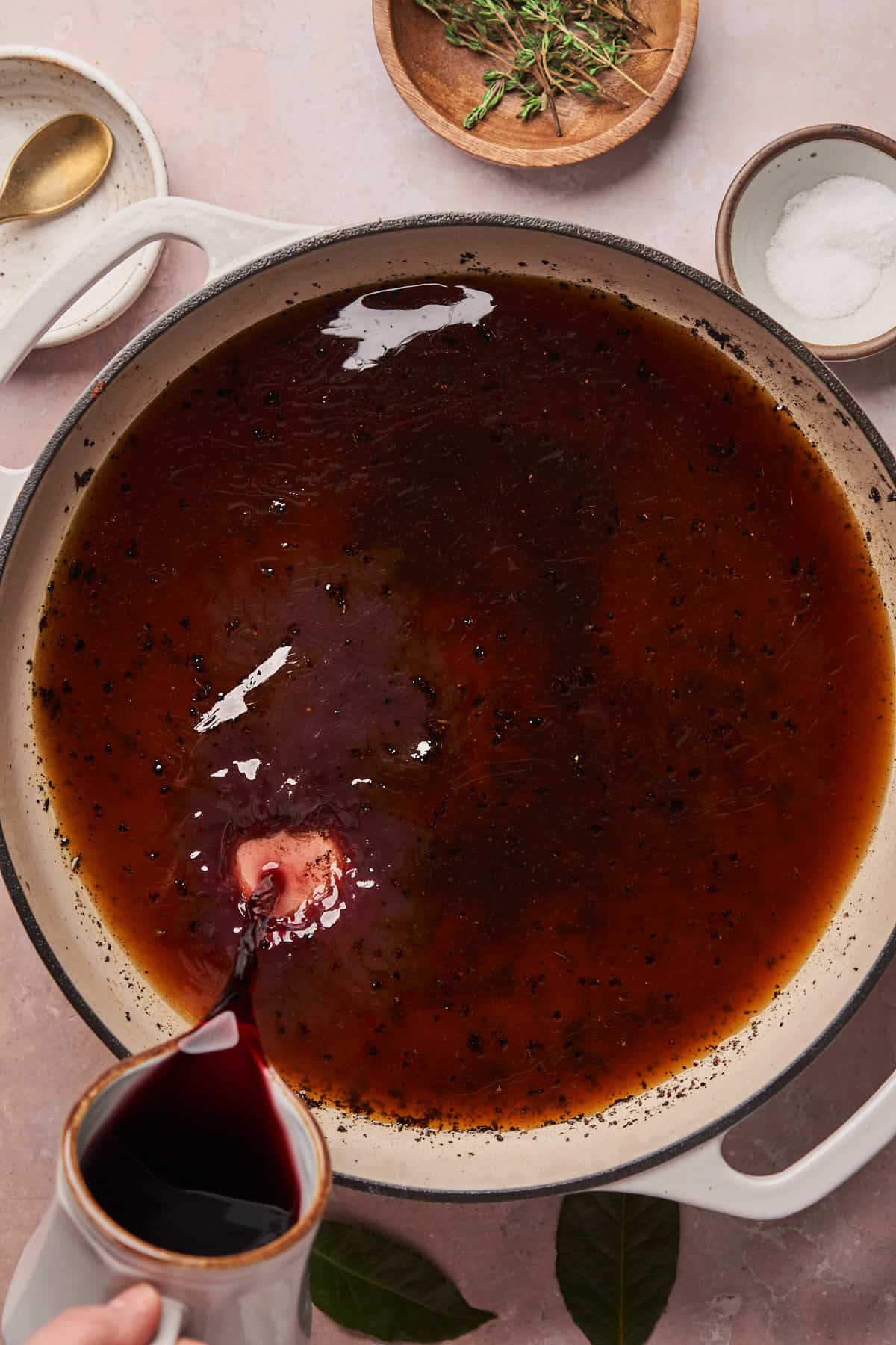 adding red wine to a braising liquid in a cast iron skillet.