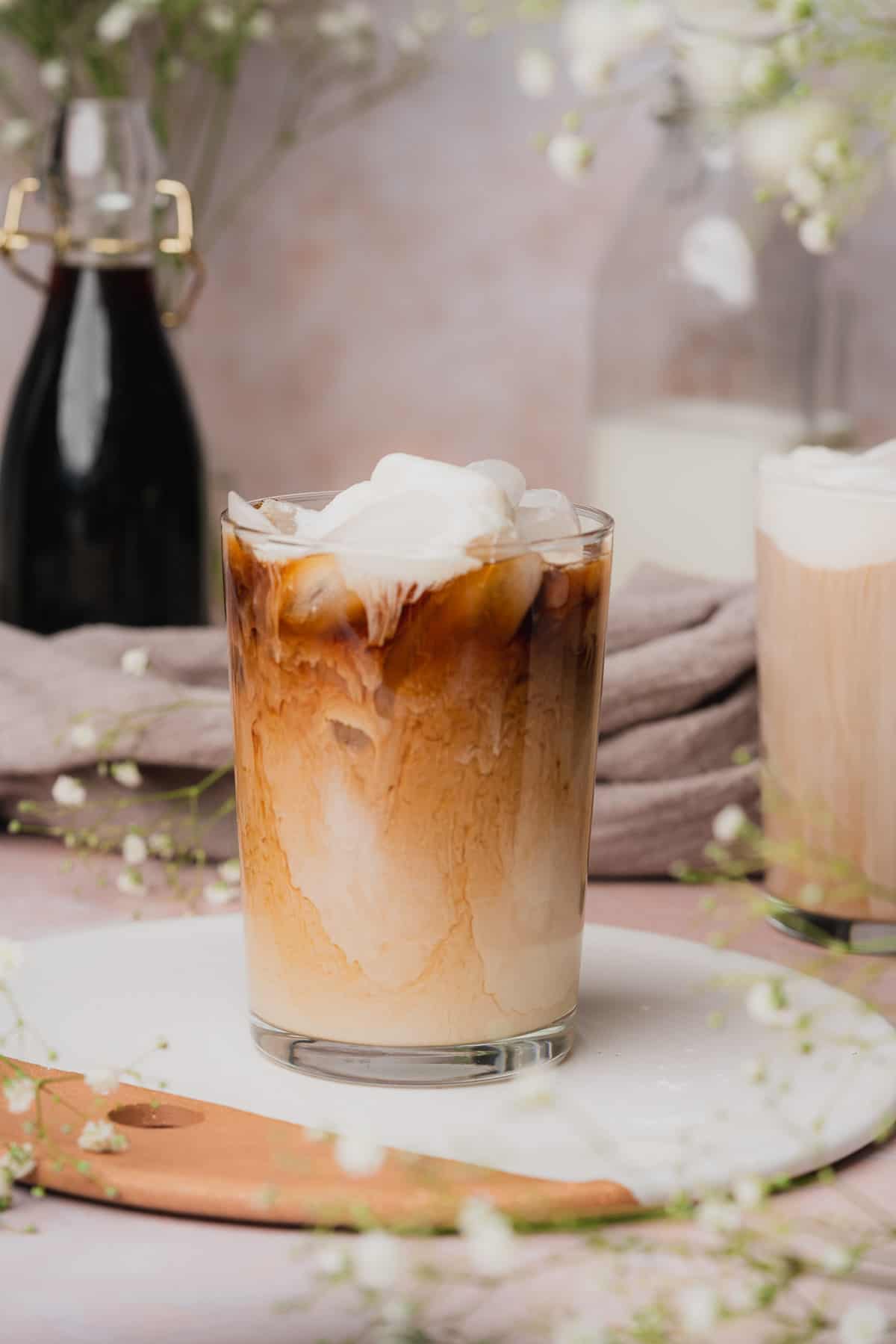 photo of an iced sweet cream cold foam coffee surrounded by small white baby's breath flowers and coffee in the background.