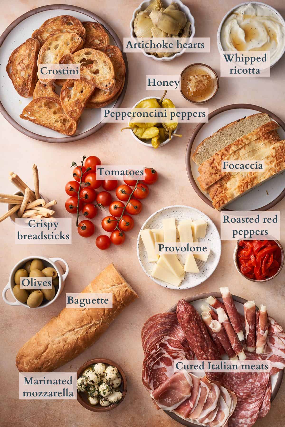 italian antipasto platter with ingredients laid out on plates with text overlaying to denote each ingredient. 