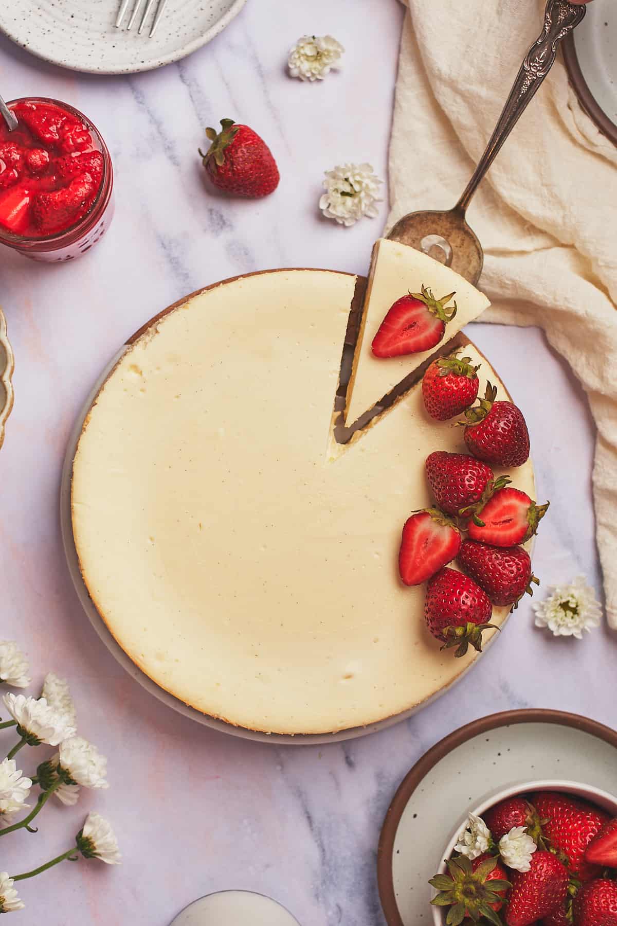 keto cheesecake recipe with fresh strawberries on top with a slice of the cheesecake being taken out. 