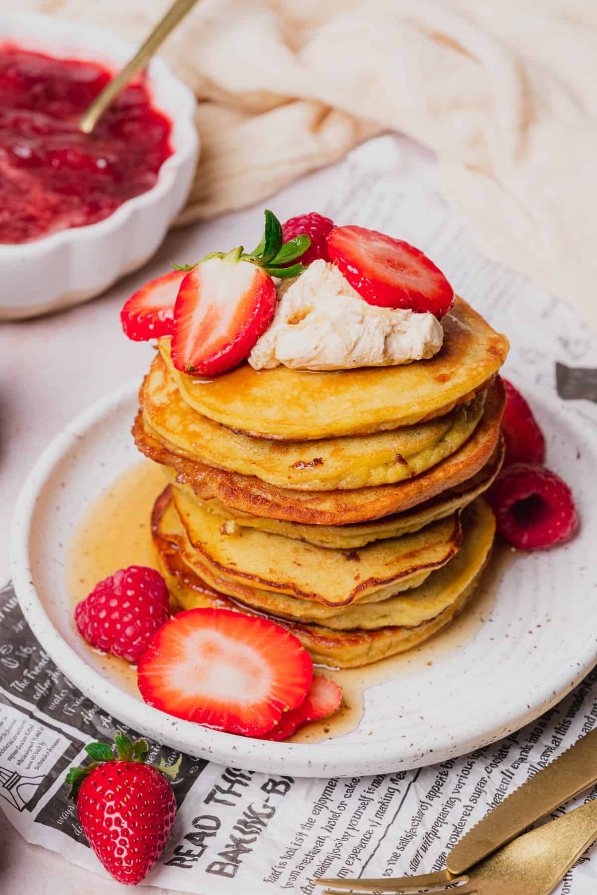 tall stack of golden brown keto coconut flour pancakes topped with whipped butter, sugar free maple syrup and strawberries