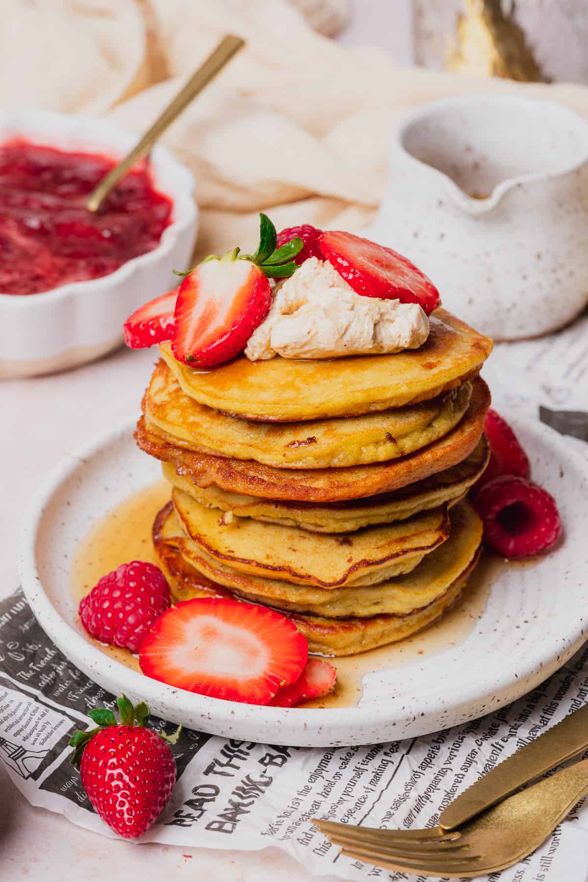 beautiful stack of fluffy coconut flour pancakes with whipped butter, maple syrup, strawberries and raspberries 