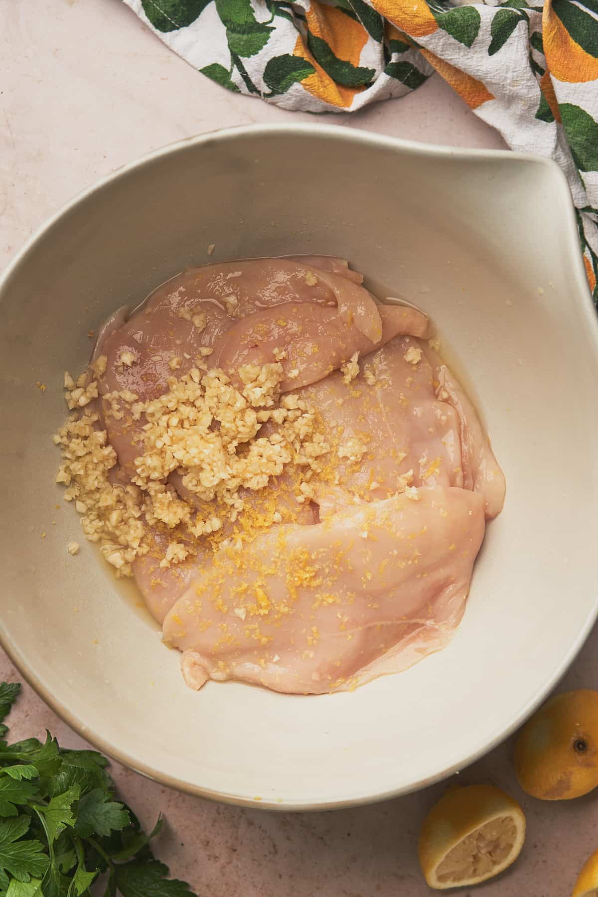 raw chicken breasts in a large white bowl with lemon juice, zest, and fresh garlic. 