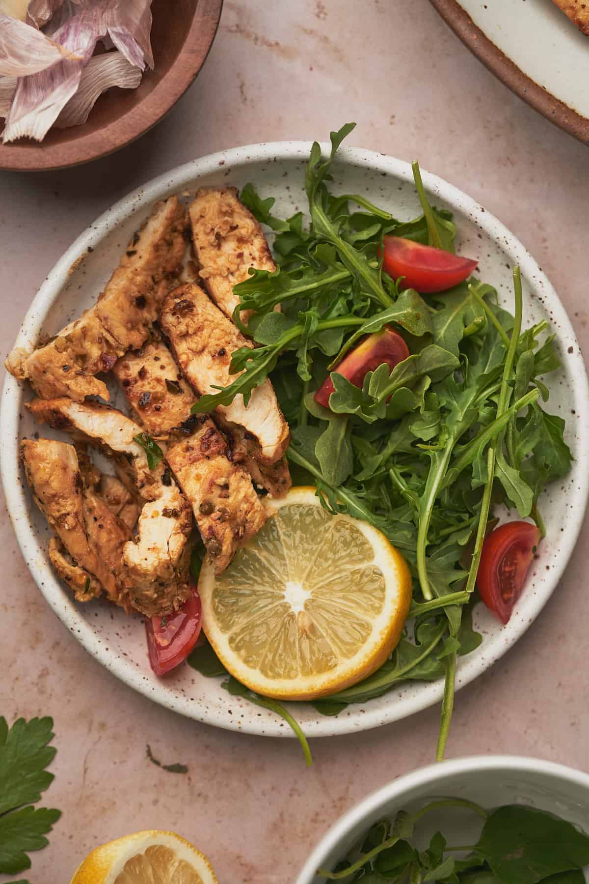 close up shot of cut up lemon herb chicken with an arugula side salad with tomatoes. 
