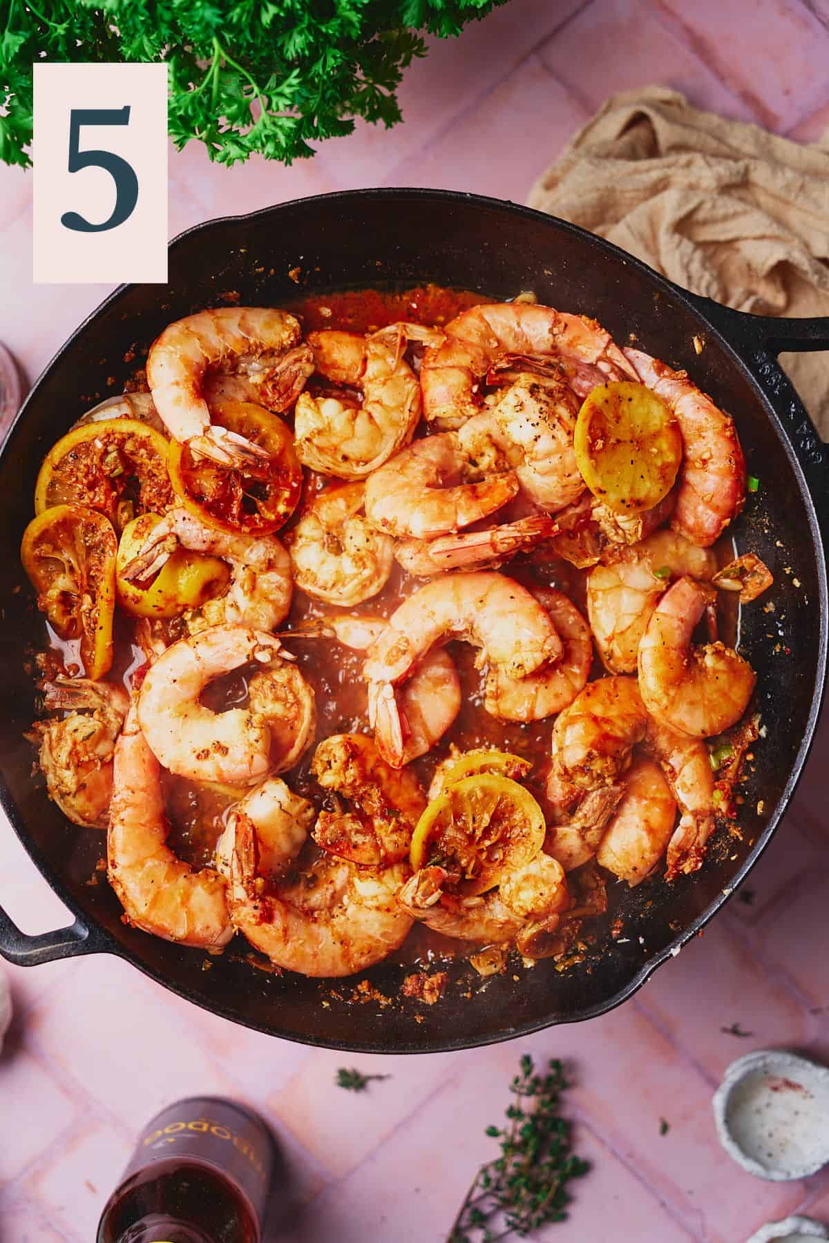 Cooked shrimp in a skillet with a bright red sauce and lemon rounds. 