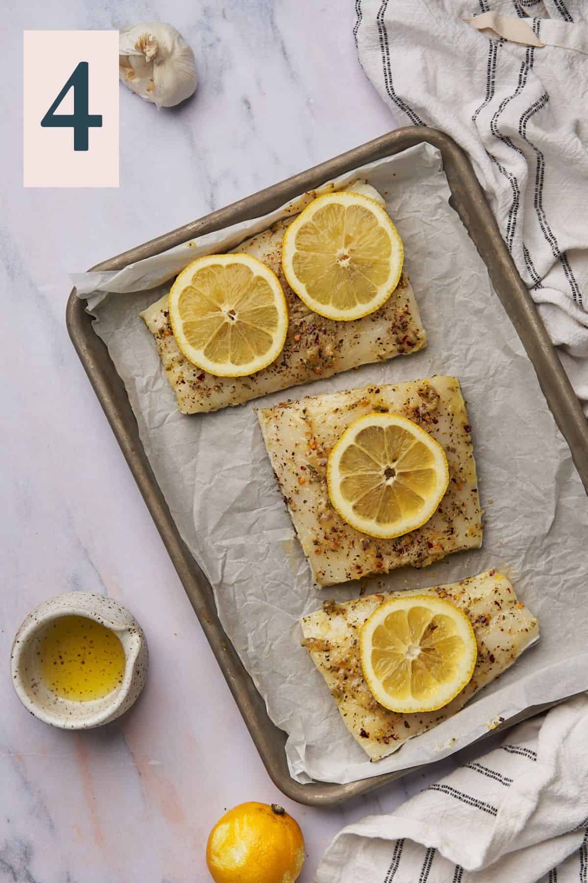 chilean sea bass fillets seasoned and topped with lemon slices on a baking sheet lined with parchment paper. 