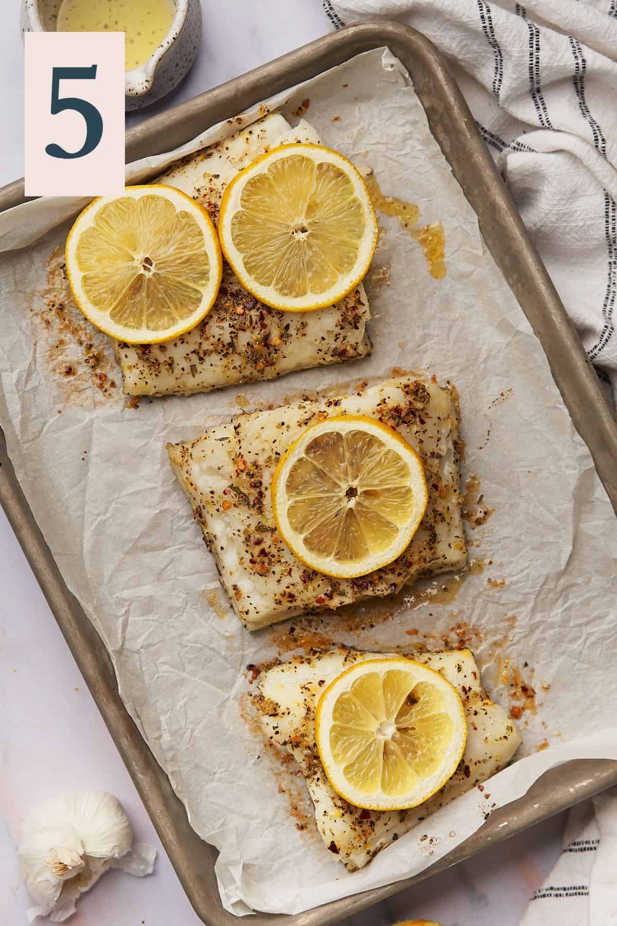cooked chilean sea bass with lemon slices on top on a baking sheet lined with parchment paper. 