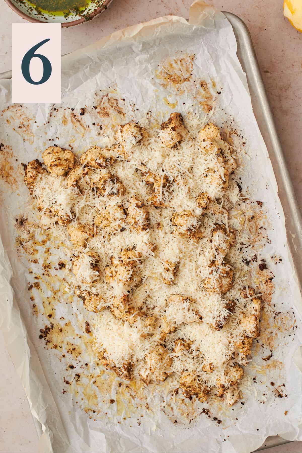 roasted cauliflower covered in freshly grated parmesan cheese on a parchment lined baking sheet.