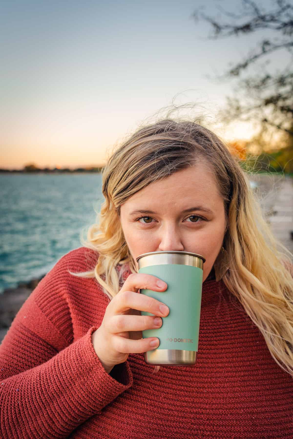 photo of woman sipping from a teal tumbler by the water at a picnic date