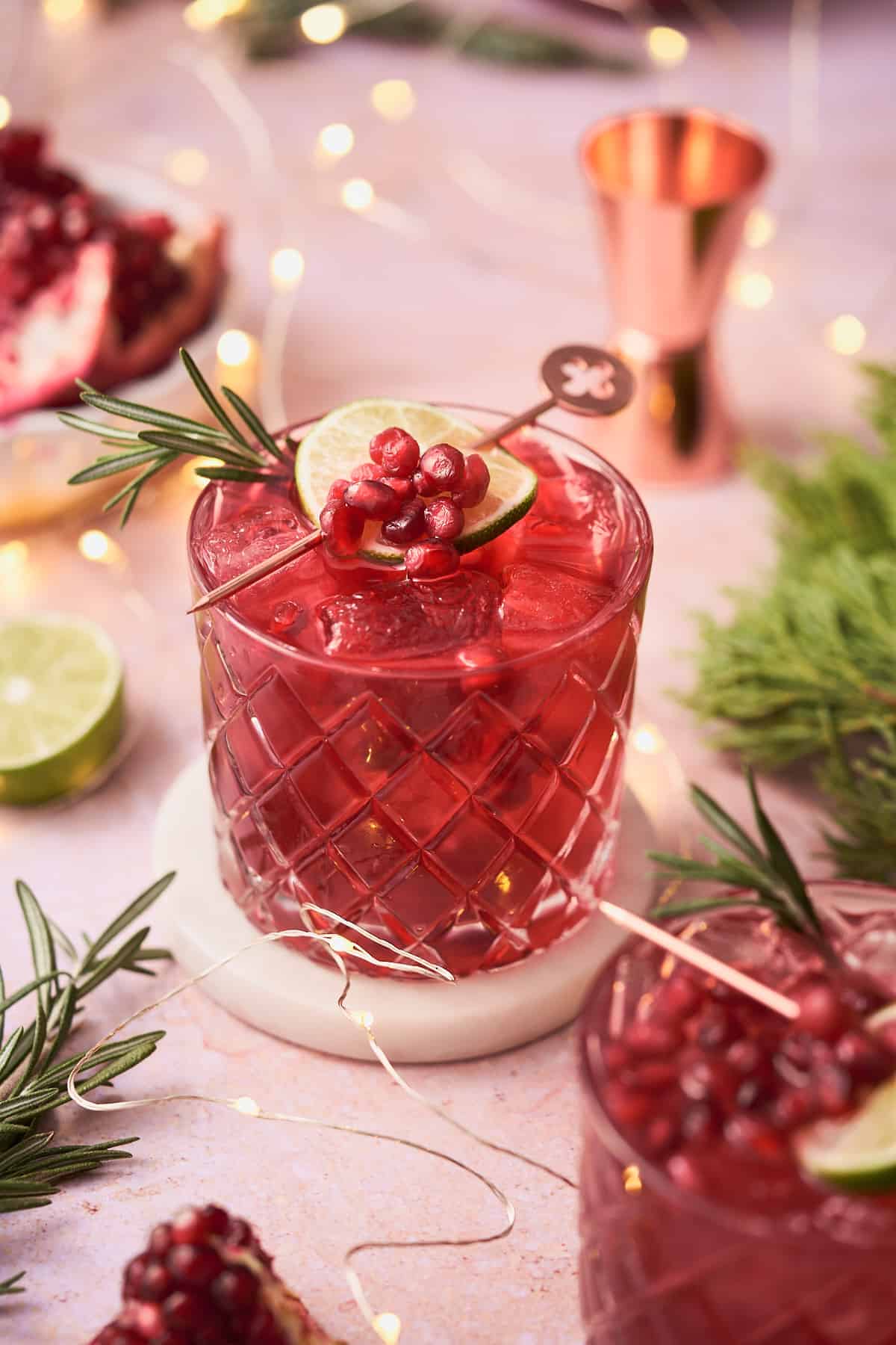 pomegranate gin cocktails with rosemary sprigs, pomegranate arils, and lime wheels as garnish, and twinkling lights on the scene. 