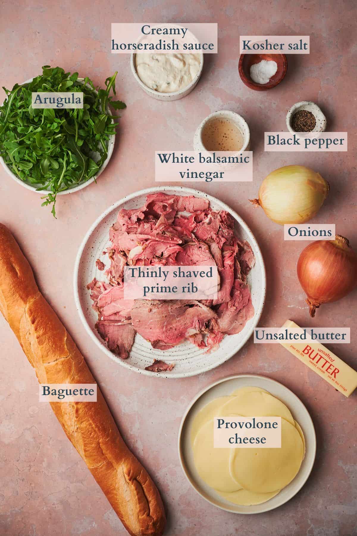 Ingredients to make a prime rib sandwich laid out on a table in small bowls and labeled to denote each ingredient. 