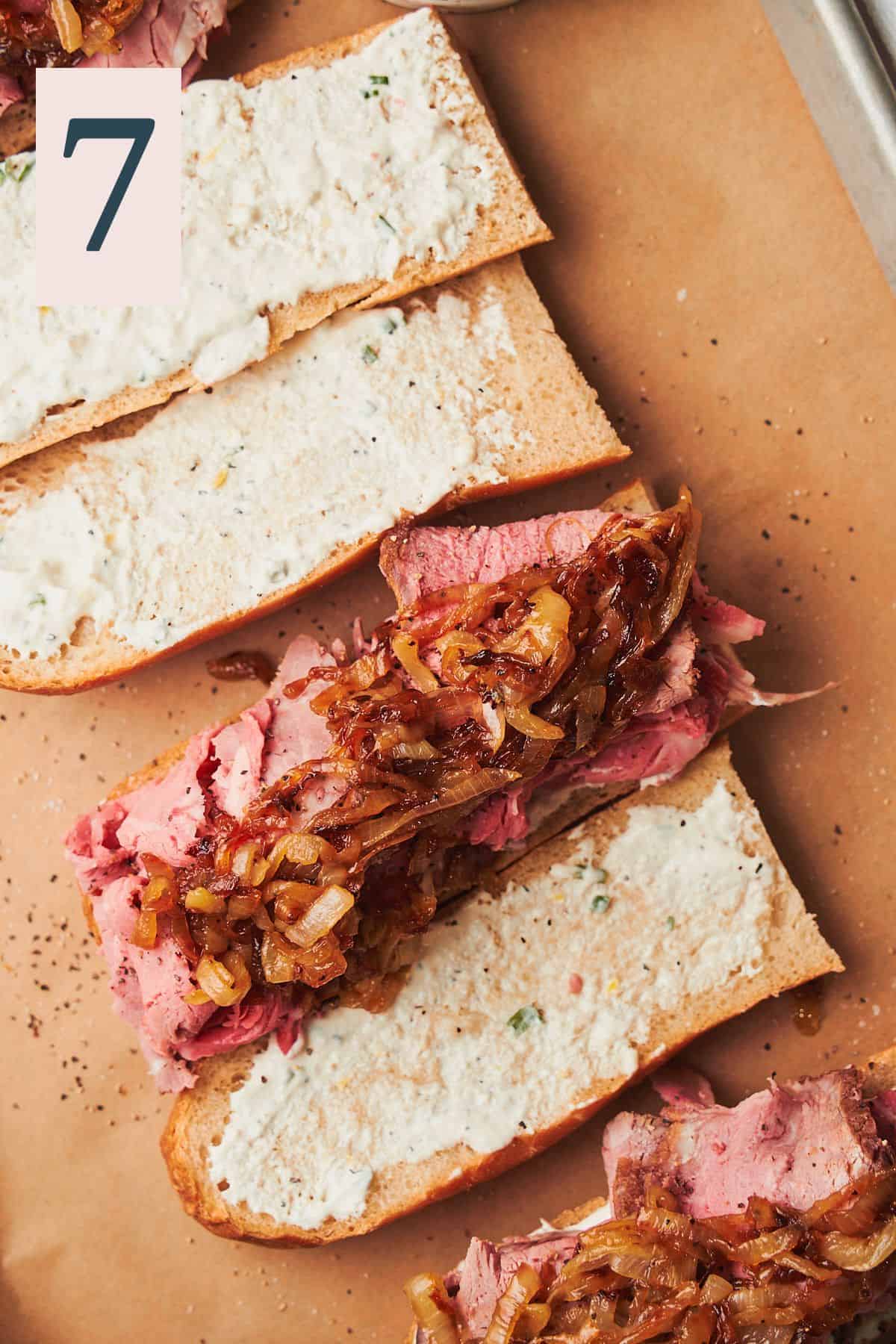 baguette sliced in half lengthwise with horseradish sauce, prime rib slices, and caramelized onions. 