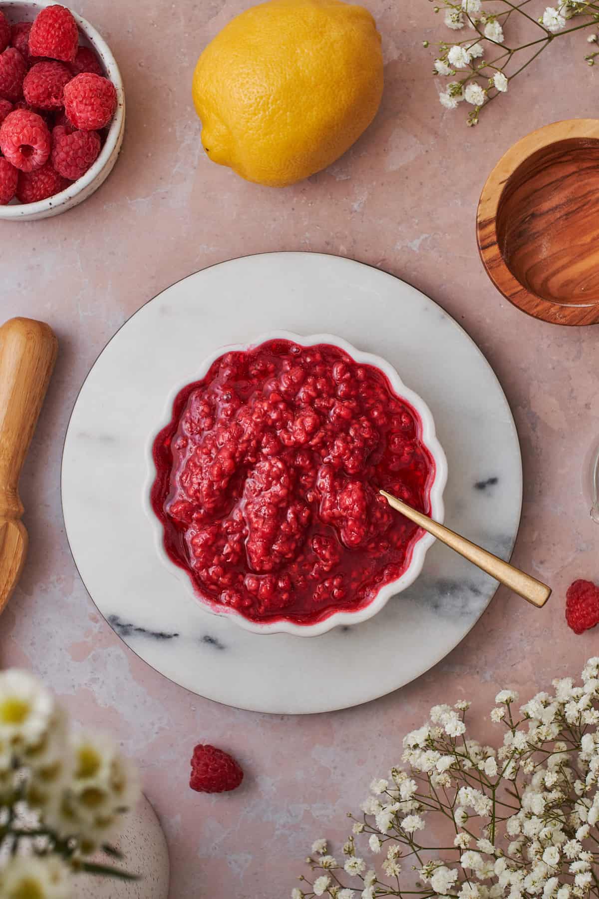 raspberry compote in a ruffled bowl, surrounded by white flowers, lemons, and fresh raspberries 