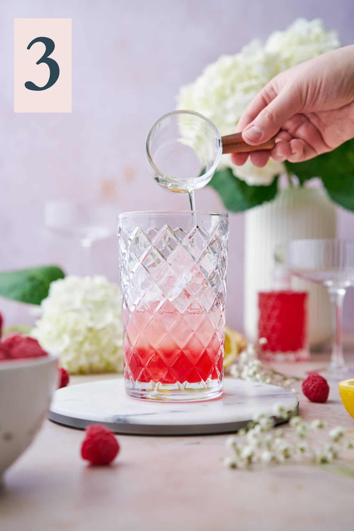 hand pouring vodka into a cocktail shaker with raspberry simple syrup. 