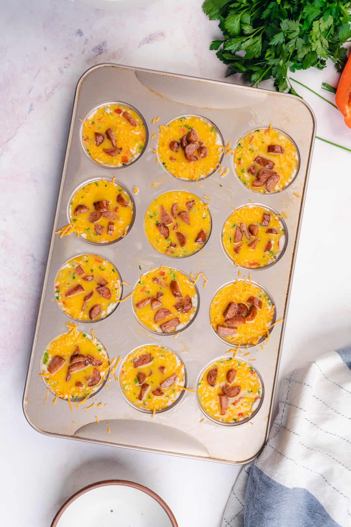 muffin tin with fill raw eggs, sausage and cheese