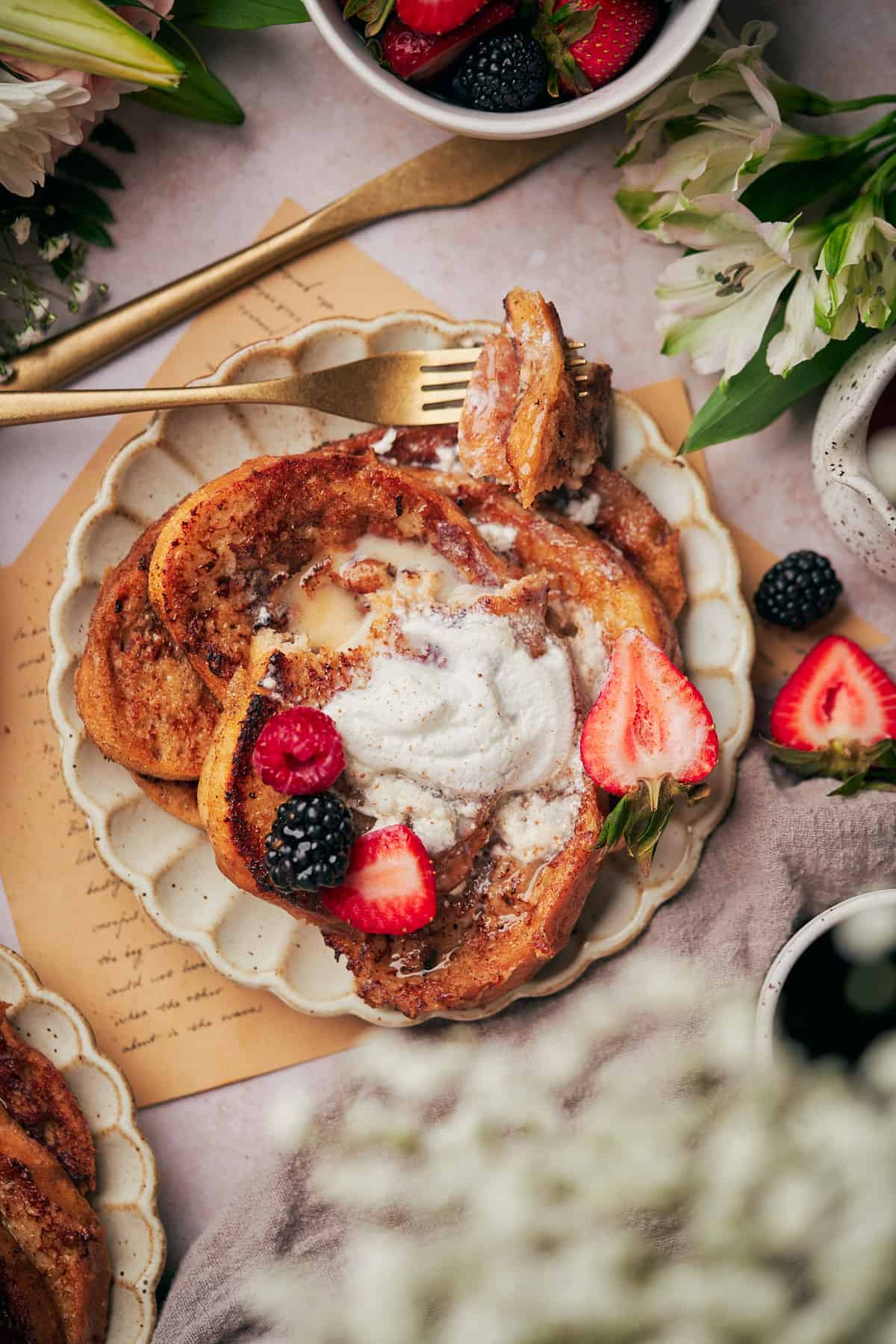 plate of sourdough french toast with fresh berries, whipped cream, and flowers surrounding it, and a letter underneath.